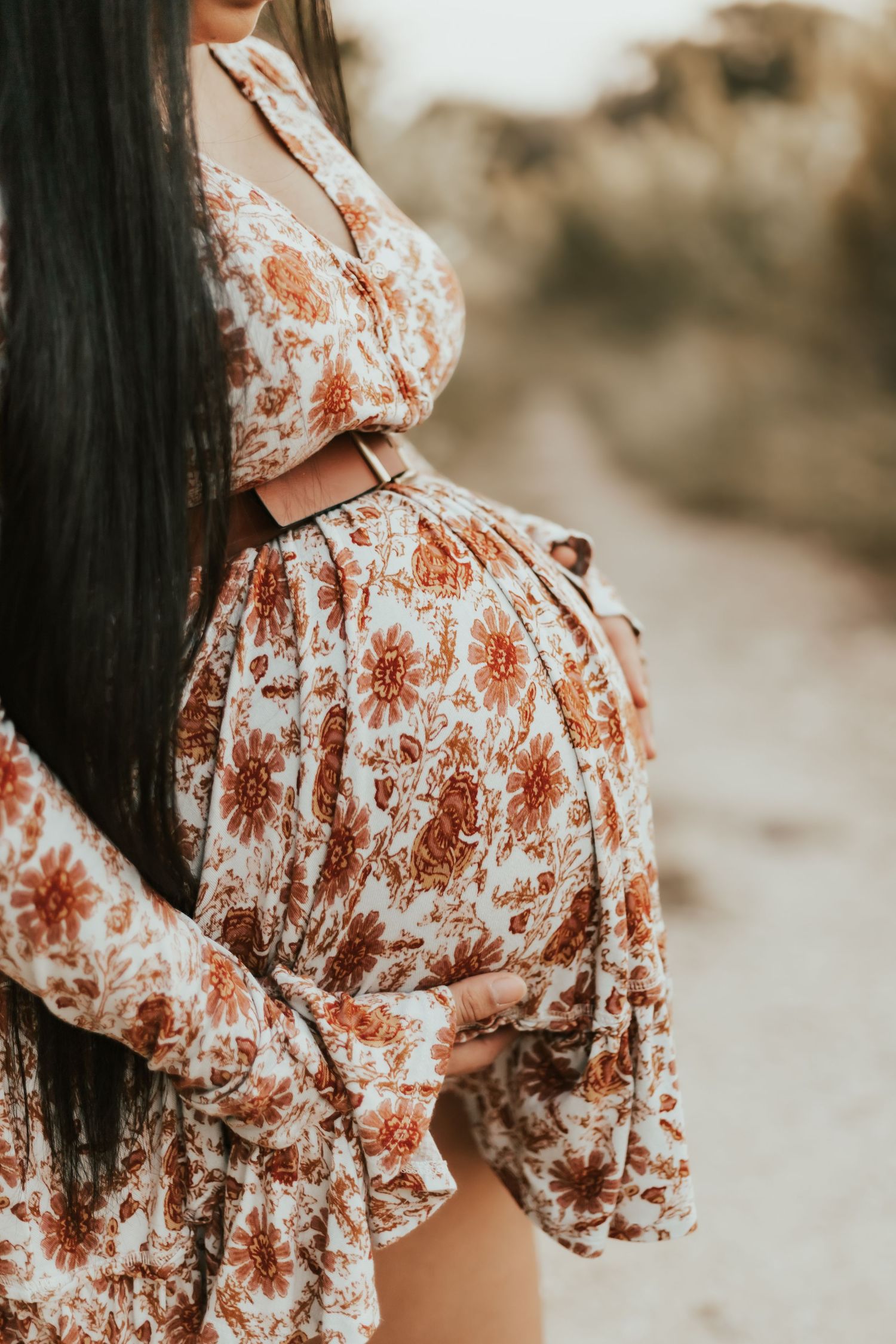 A close-up side view of a pregnant woman wearing a floral dress with rusty orange and cream colored print.