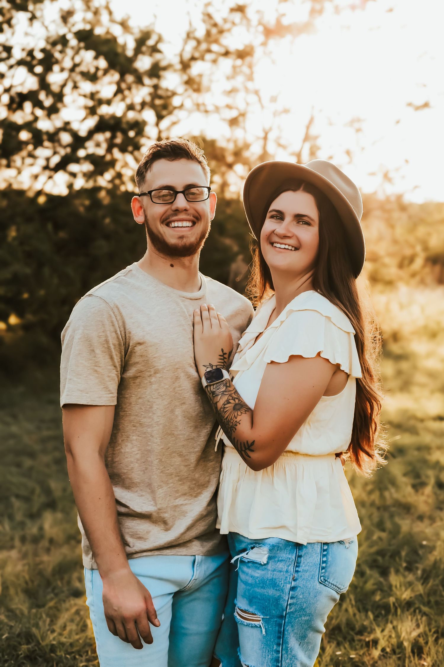 Couple enjoying sunset in casual outfits standing together outdoors during golden hour photography session.