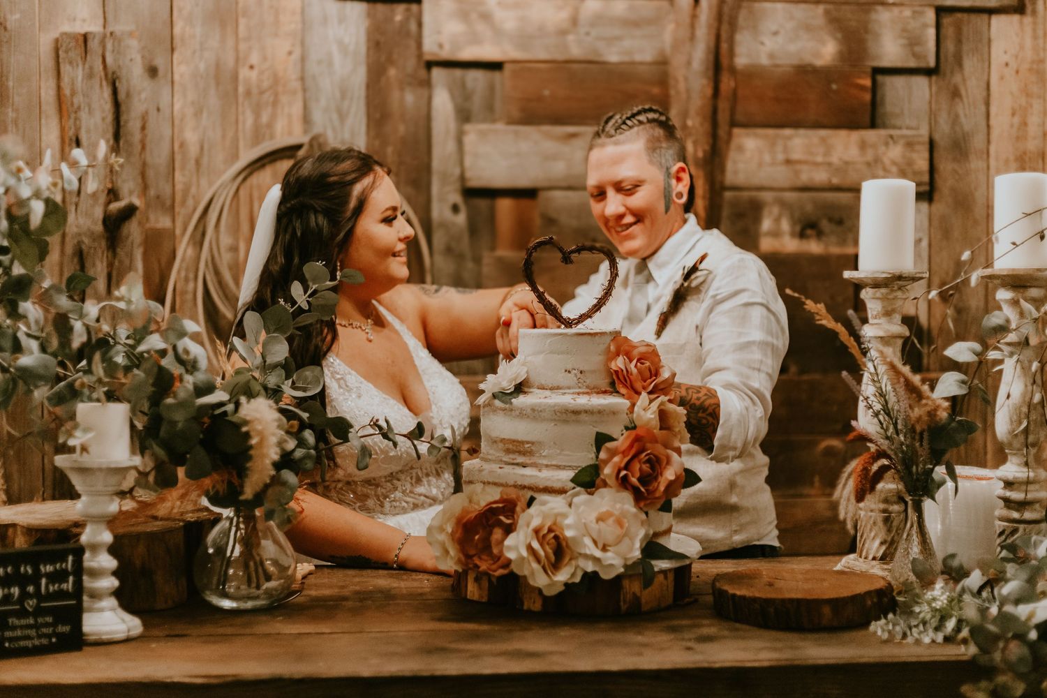 Rustic wedding reception with couple sharing intimate moment at decorated wooden table with flowers.
