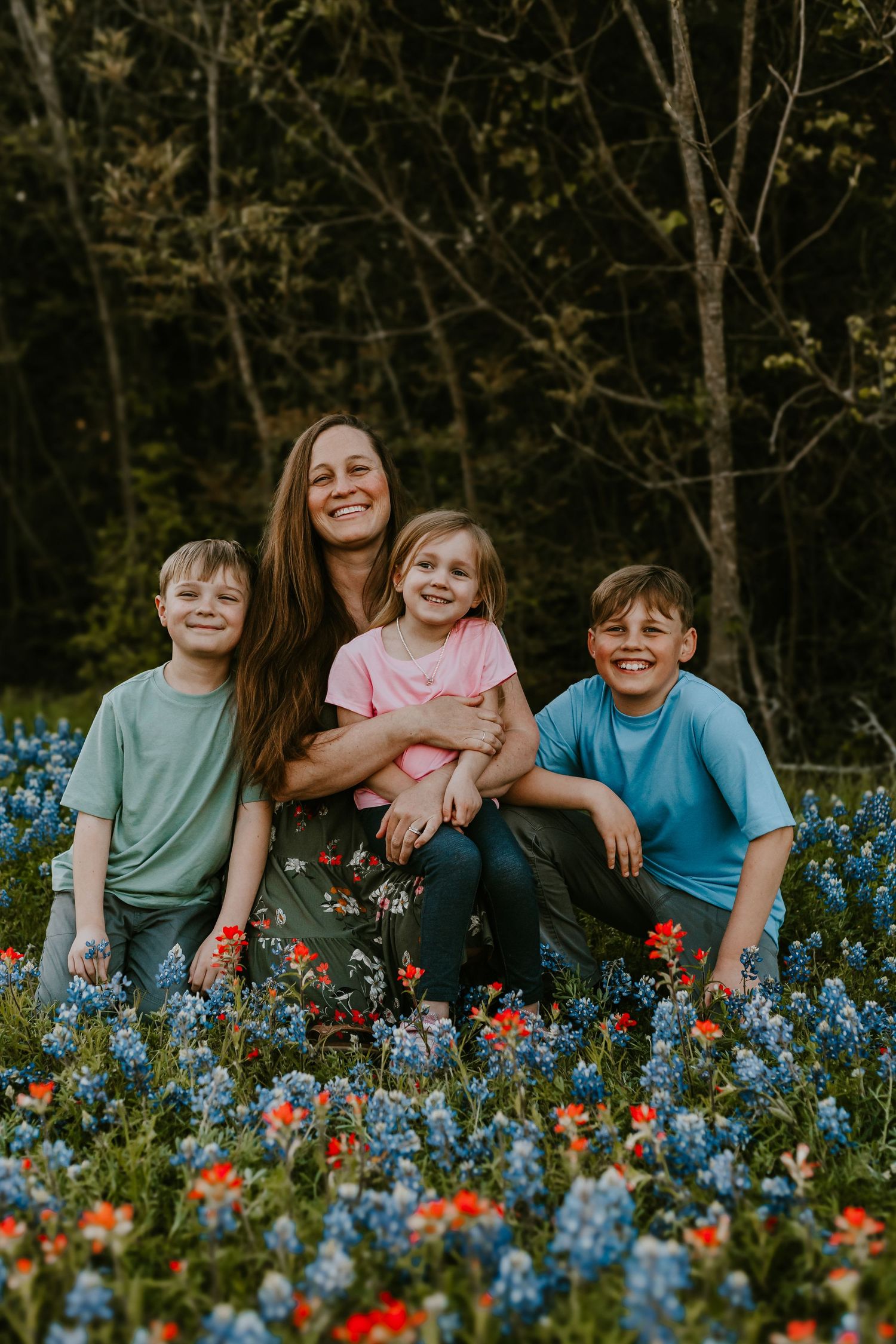 A happy group sits together in a field of vibrant bluebonnets and red wildflowers during golden hour.