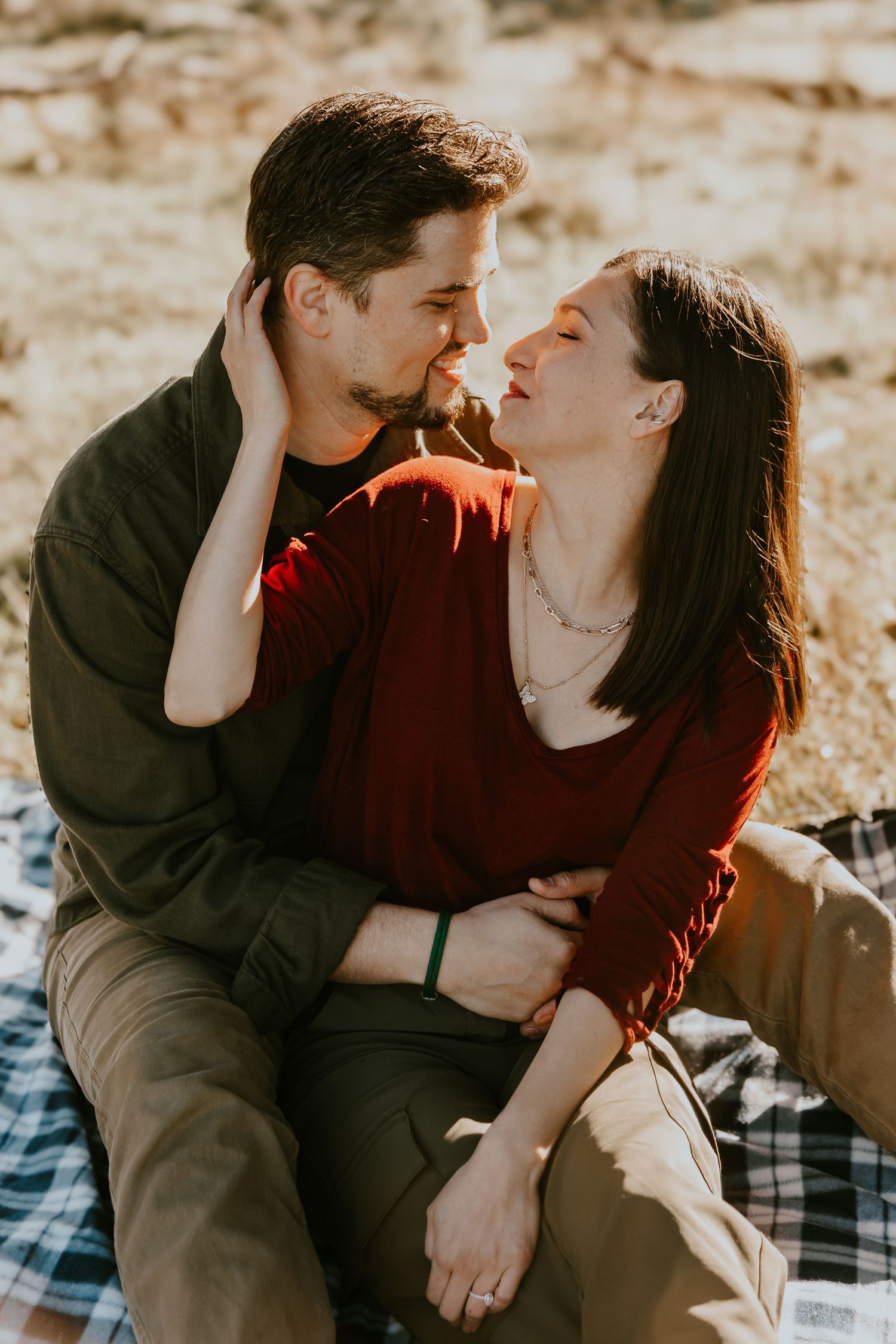Intimate couple sharing romantic moment on picnic blanket in warm sunlight outdoors.