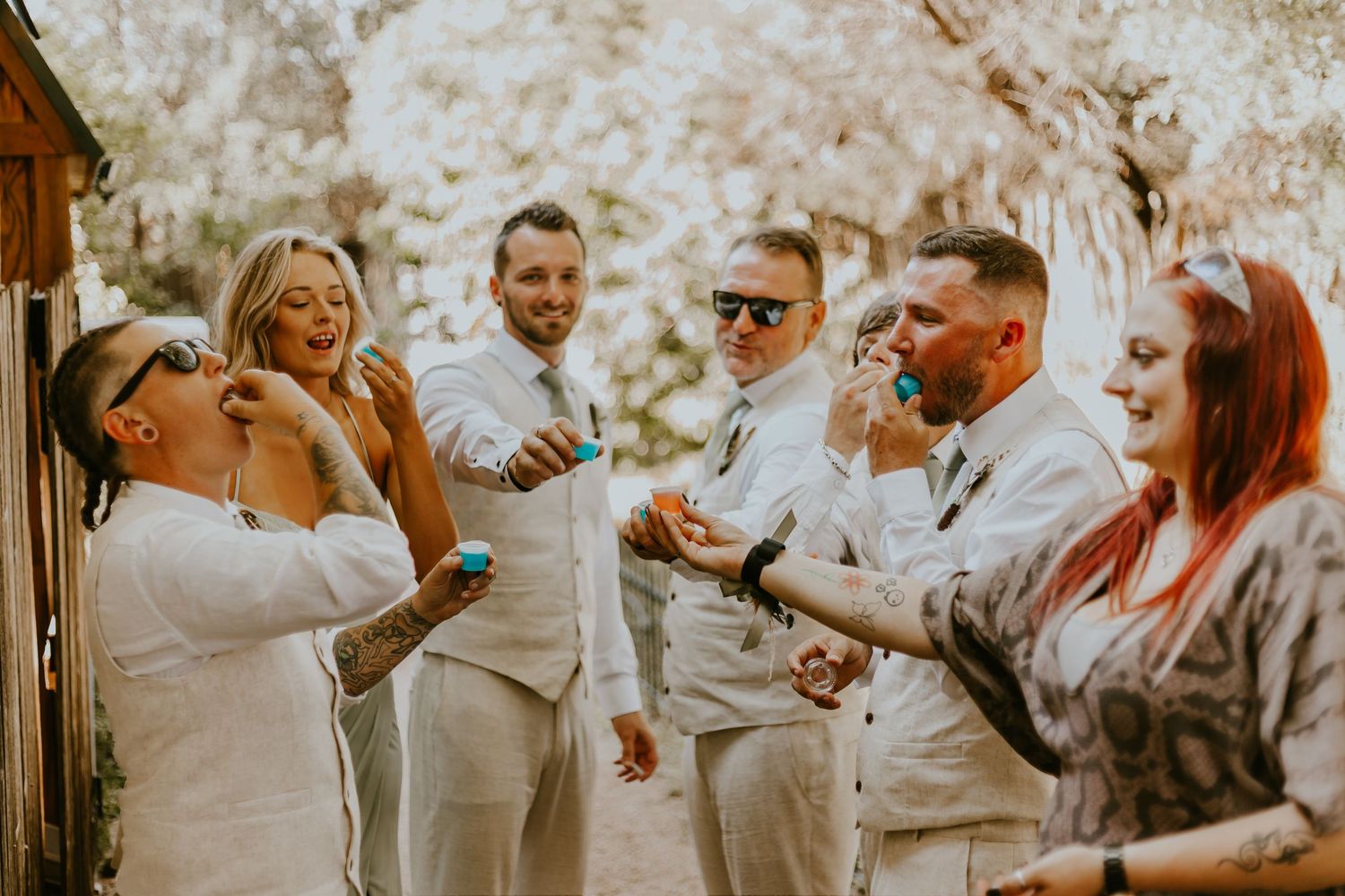Wedding party throws confetti and celebrates joyfully together outdoors in coordinated white outfits.