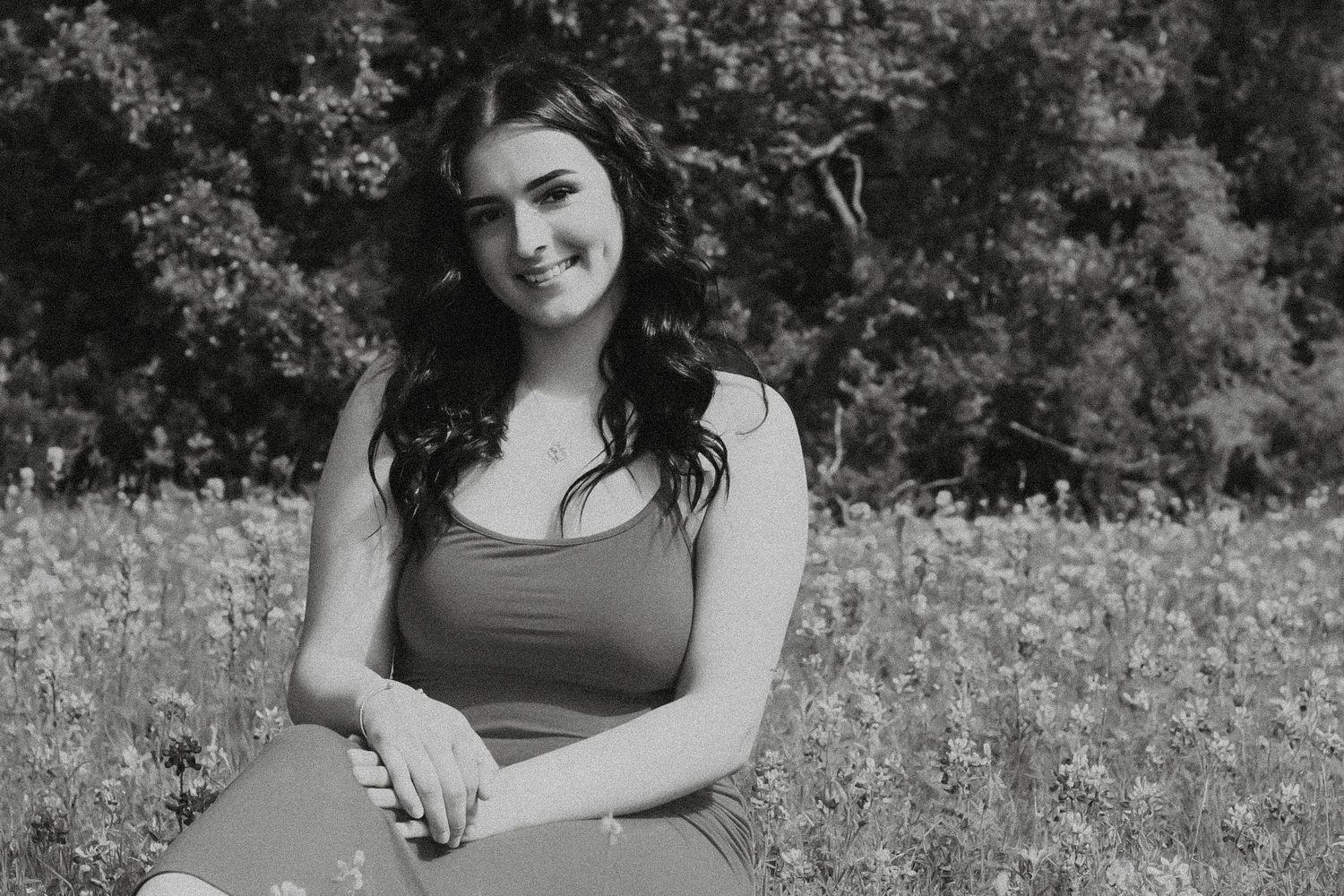 Black and white outdoor portrait of person sitting in grassy field.