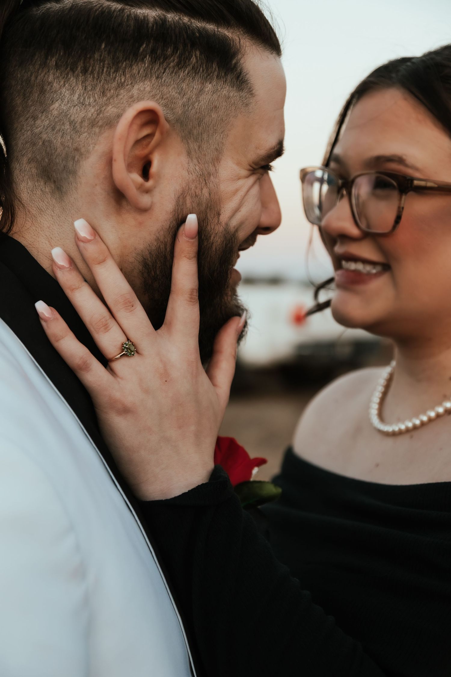 Close-up shot of a couple sharing an intimate moment, with the person in glasses wearing a pearl necklace.