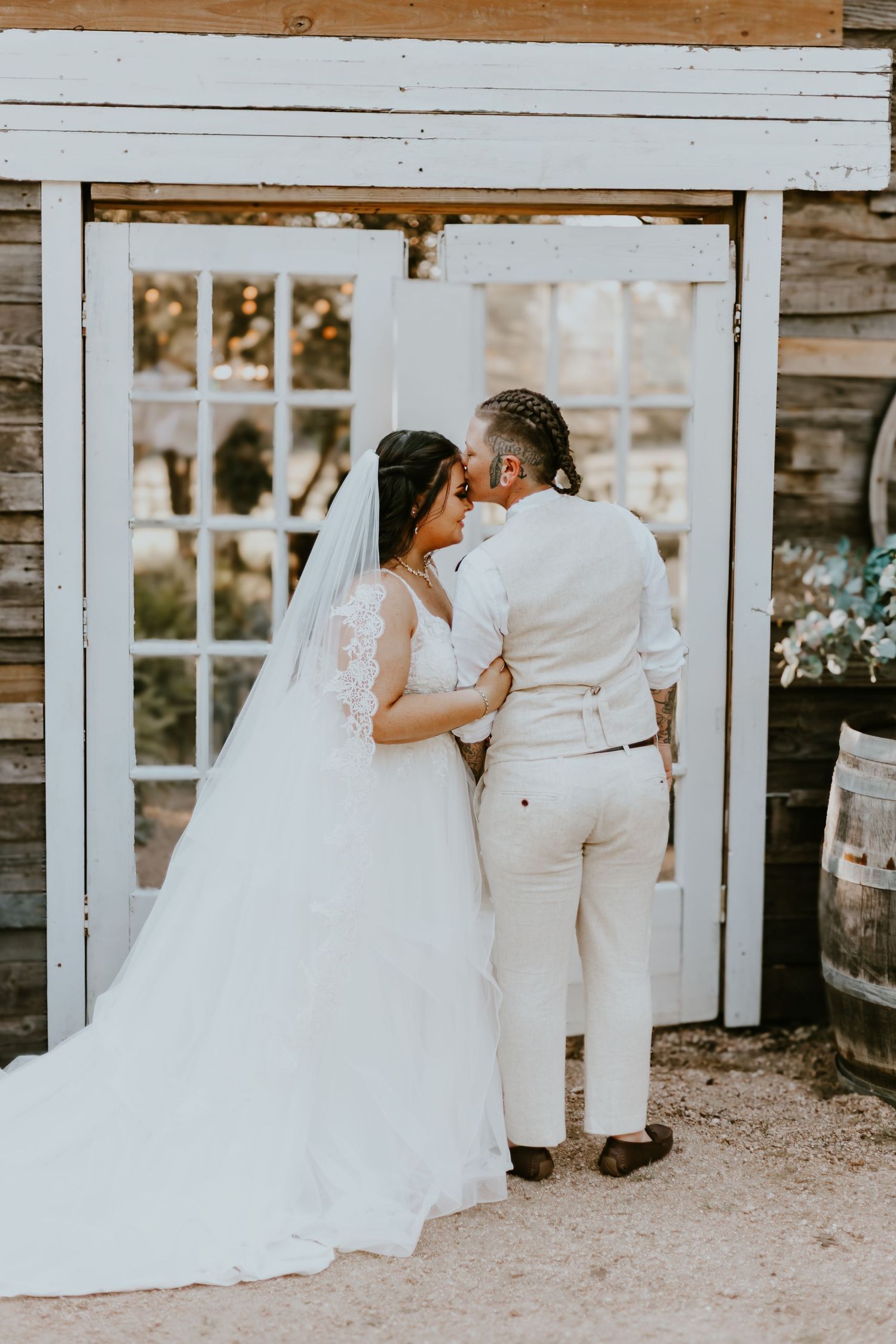 A couple shares an intimate moment together in front of a rustic white door during their outdoor wedding.