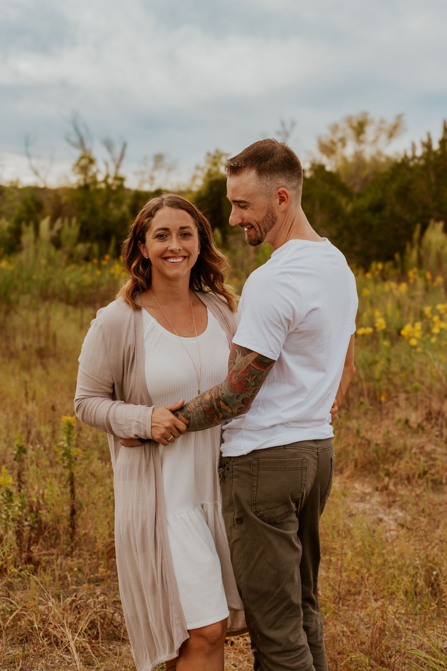 A couple embraces in a golden sunlit field during a warm autumn evening photo session.