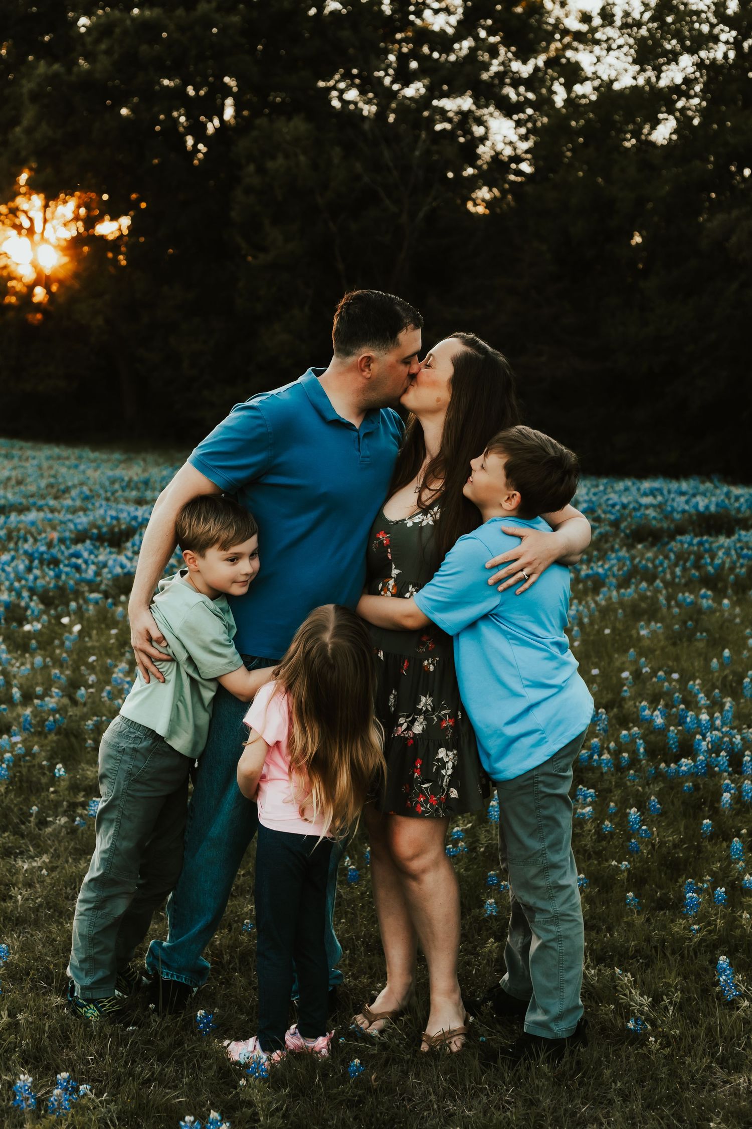 Family shares tender moment together in field of blue wildflowers at sunset in Texas countryside.