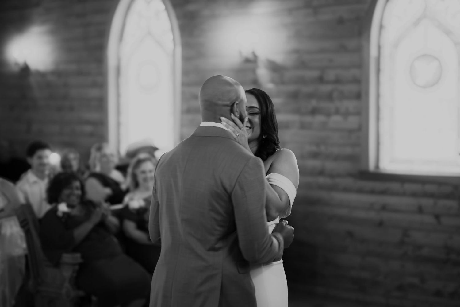 A romantic couple shares a joyful moment while dancing together at a wedding reception in a rustic chapel setting.