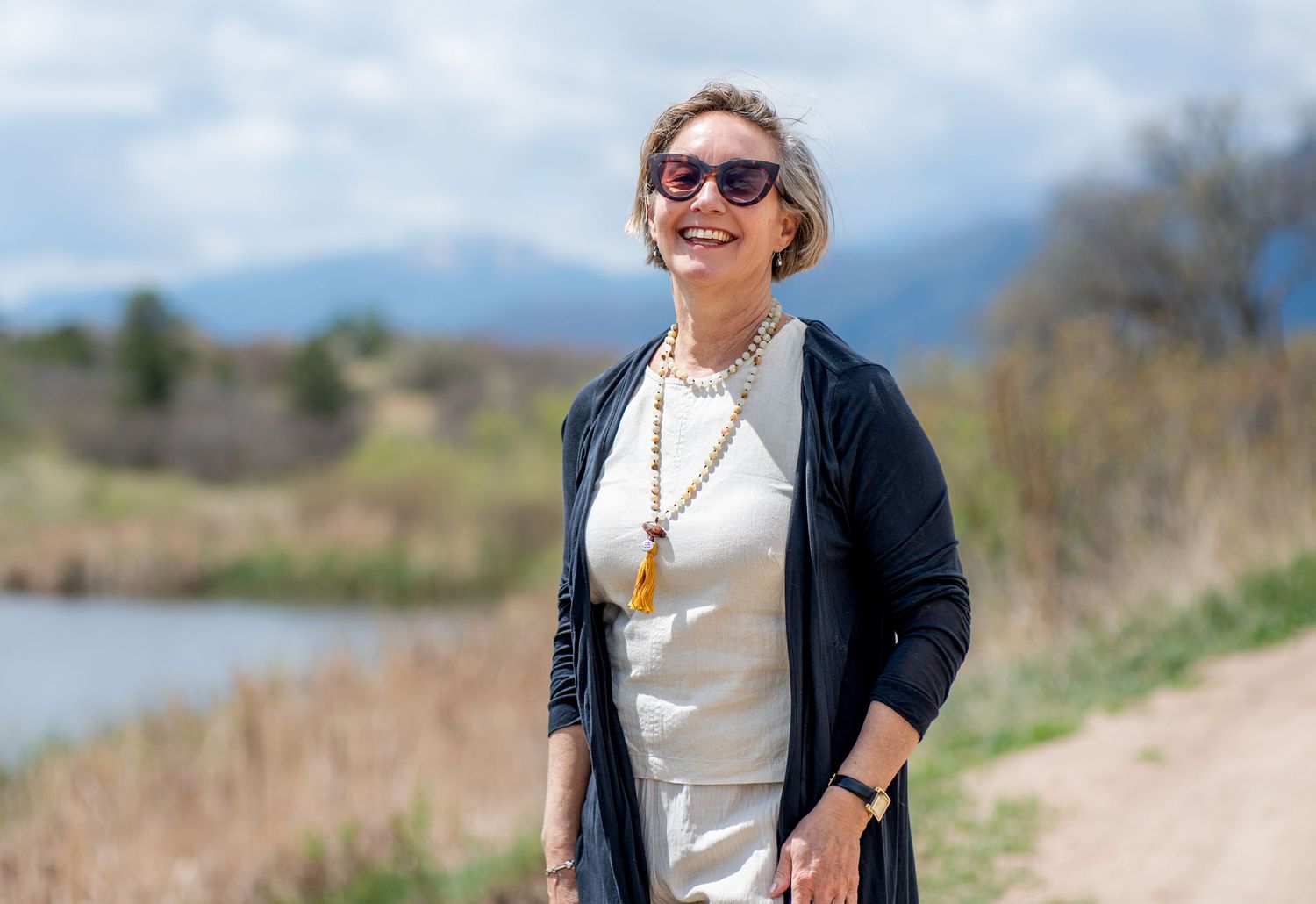 Woman in the sunshine laughing near a pond with Pikes Peak in the background
