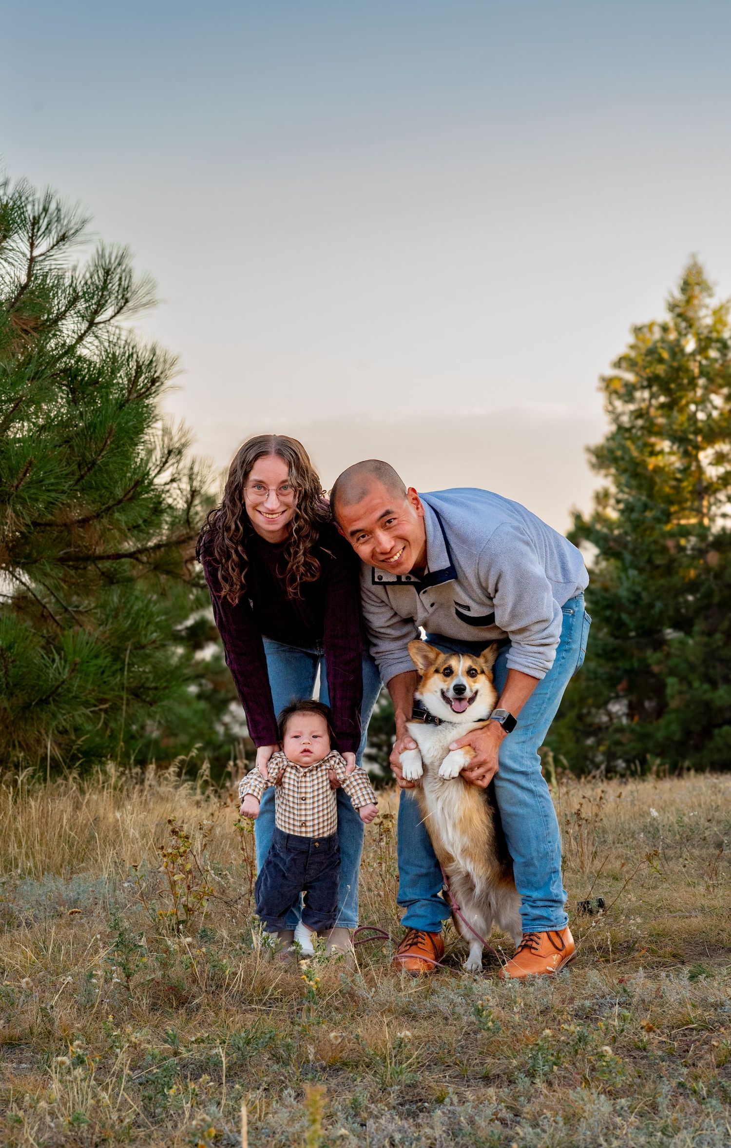 couple helping a baby and dog stand for a portrait with mountains in the background at golden hour