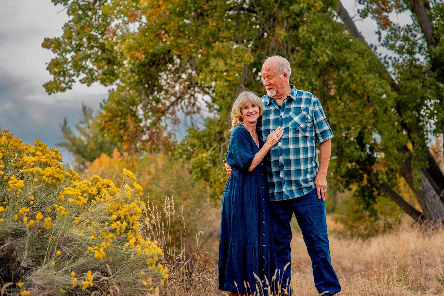 couple wearing blue outfits in front of a cottonwood tree
