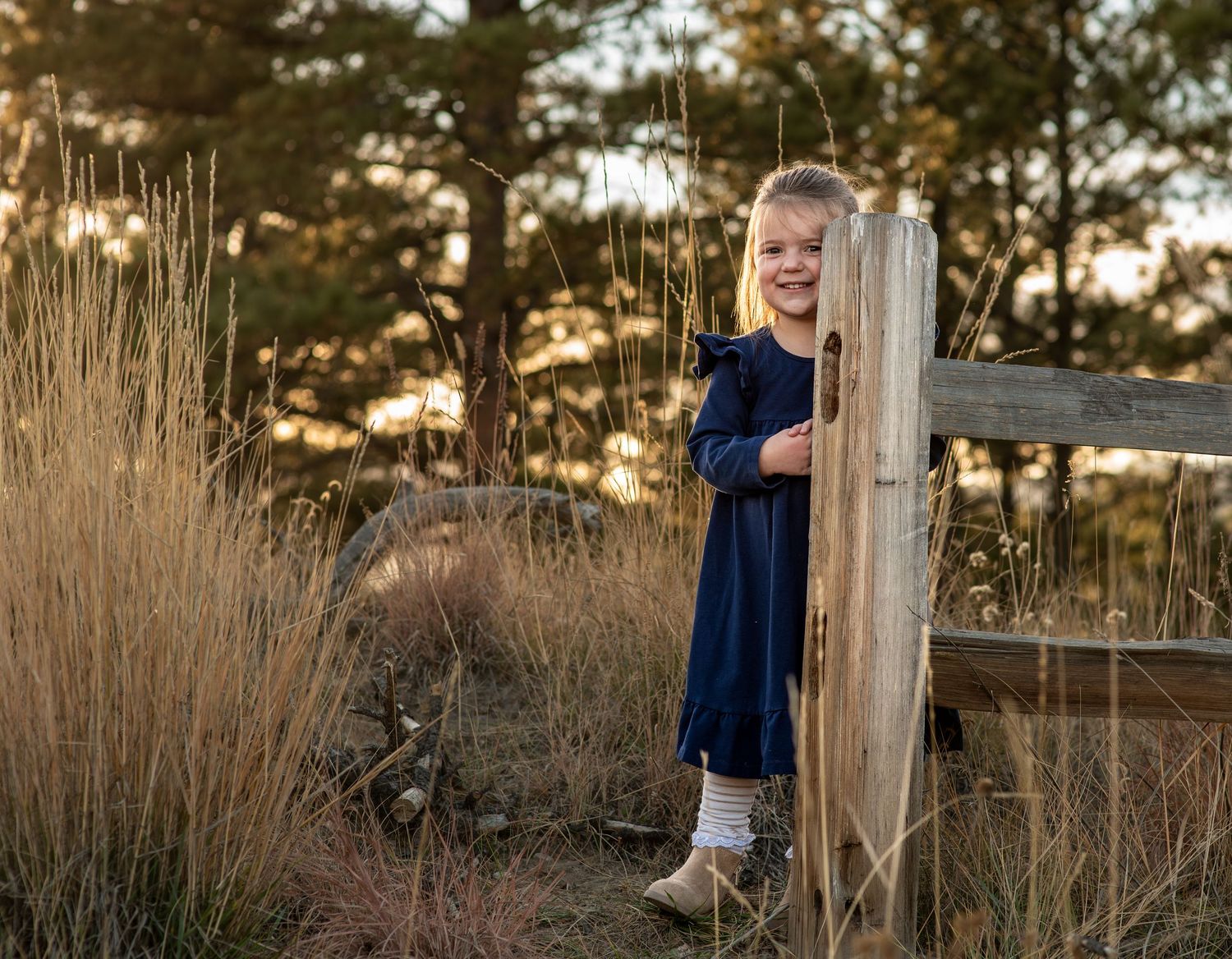 young girl peeking out from behind a fence post