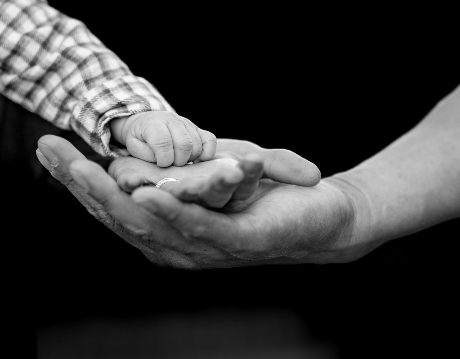 couple layering hands with babies hand on top against a black background