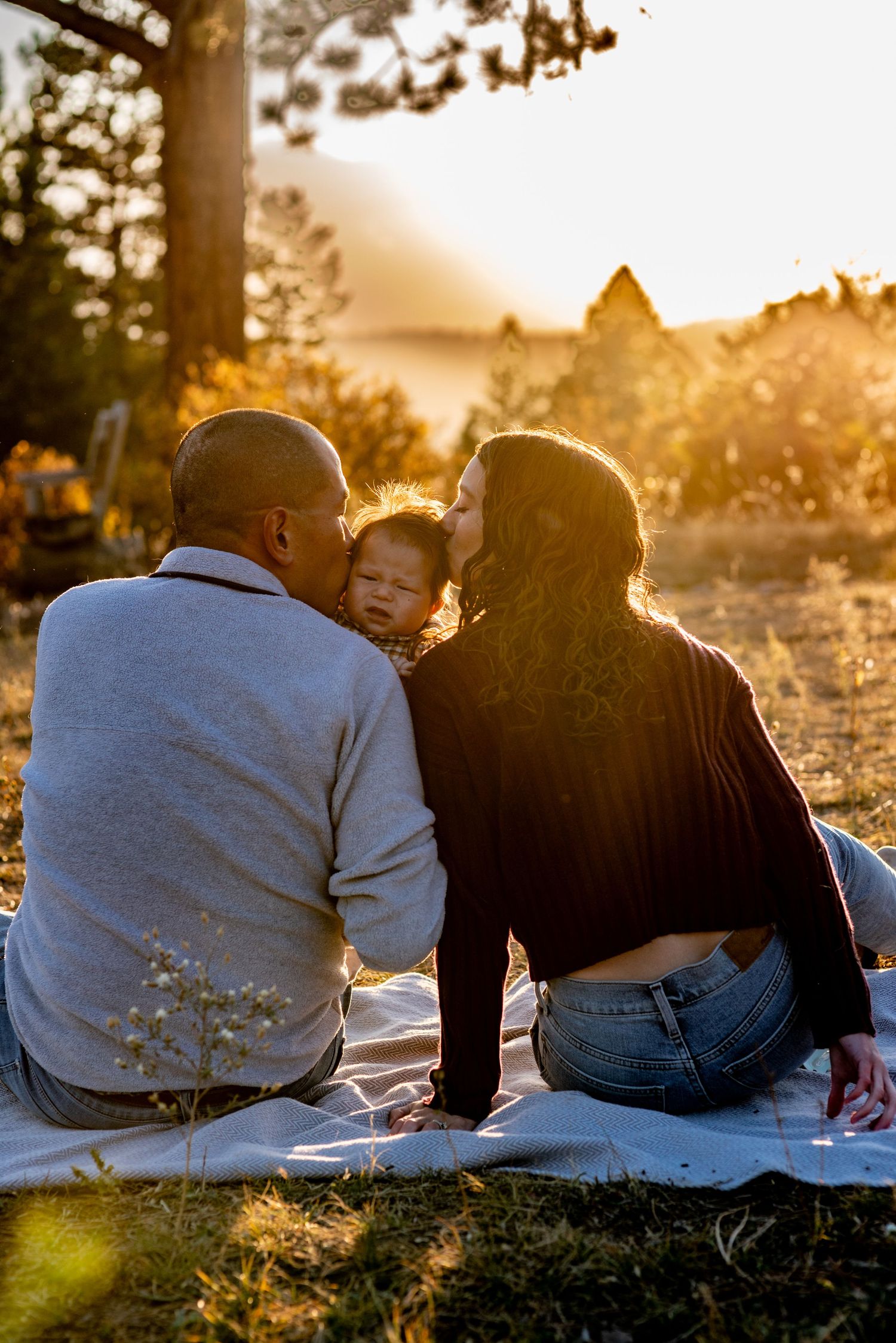 couple kissing a baby with golden hour sun in the background
