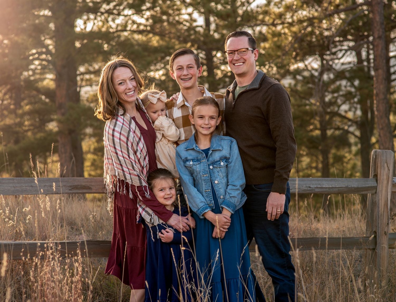 family posing at golden hour in front of a fence