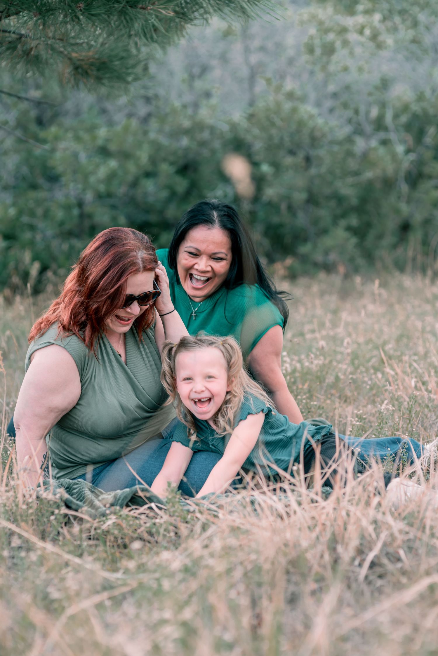 two women sitting in the grass with young girl laughing
