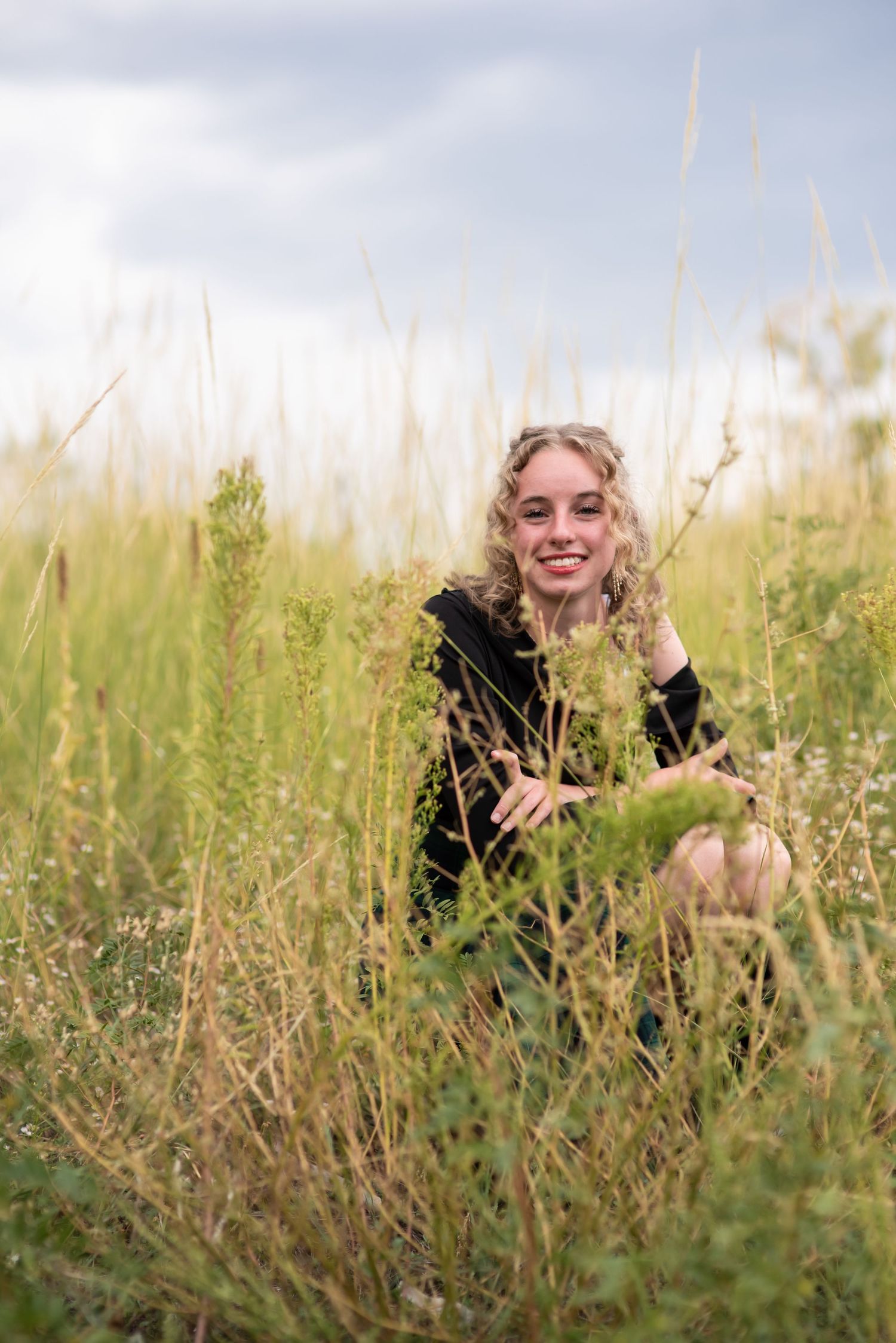 Young woman sitting in the grass with a green and blue background for senior photos