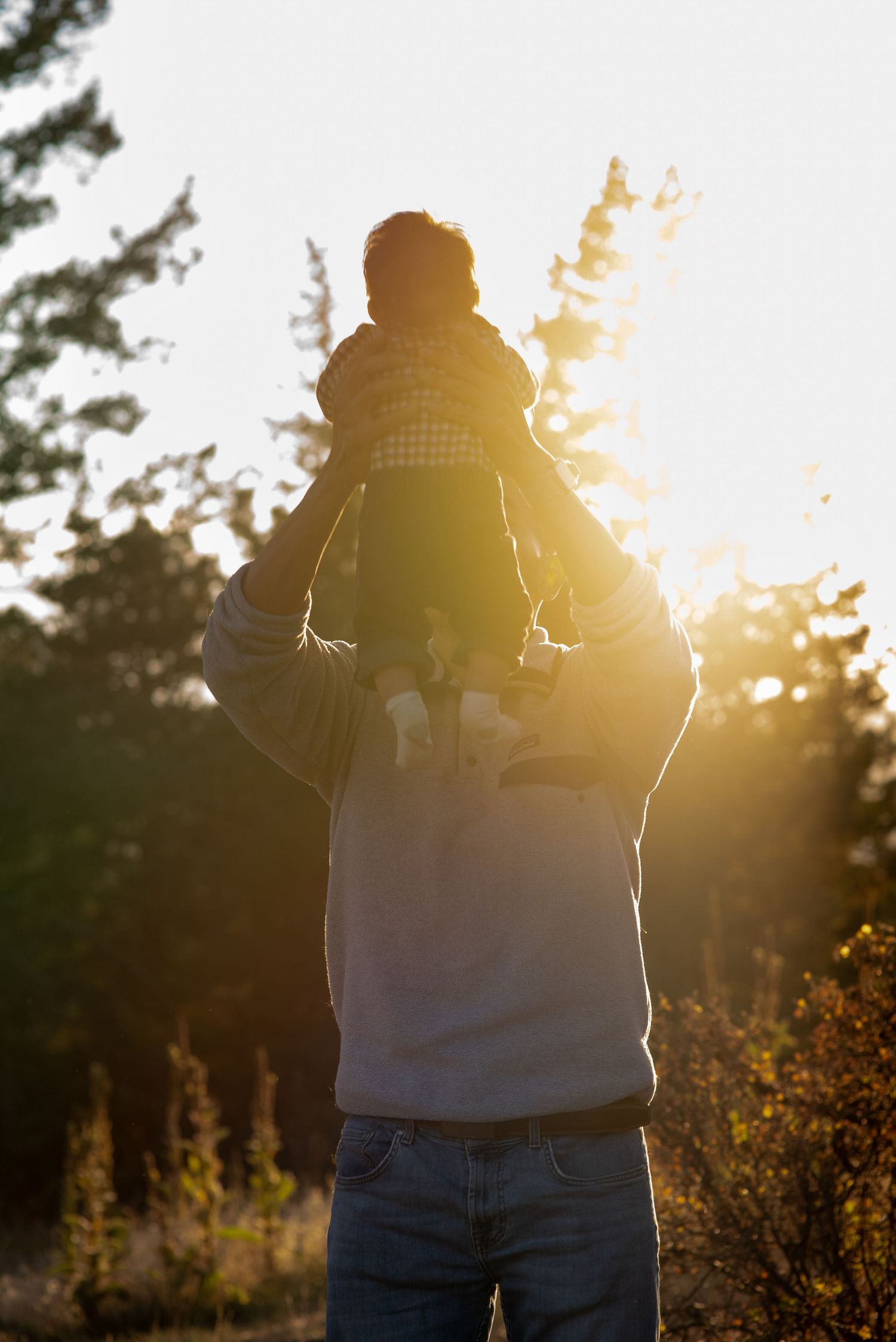 dad lifting a baby up in the air with the sun shining in the background at golden hour