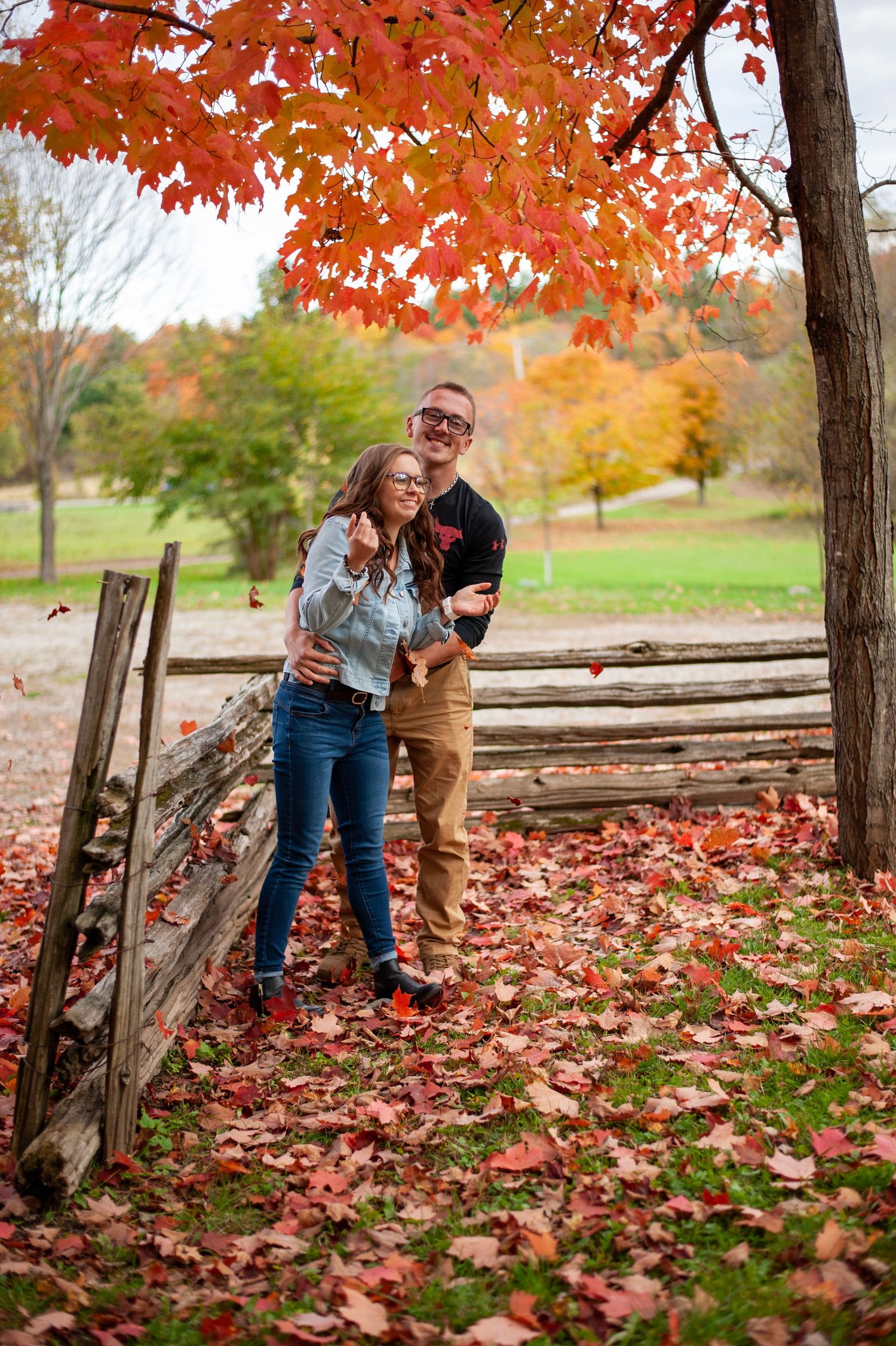 Couple enjoying fall foliage near rustic wooden fence with vibrant red maple leaves.