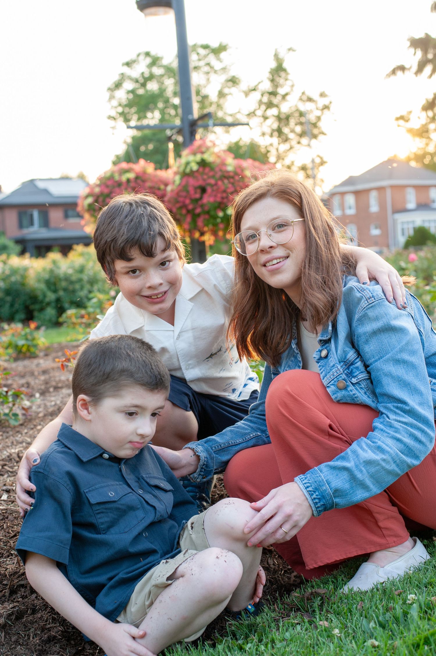 A family sits together on a grassy hill at sunset, wearing casual clothing and smiling while enjoying an outdoor moment.