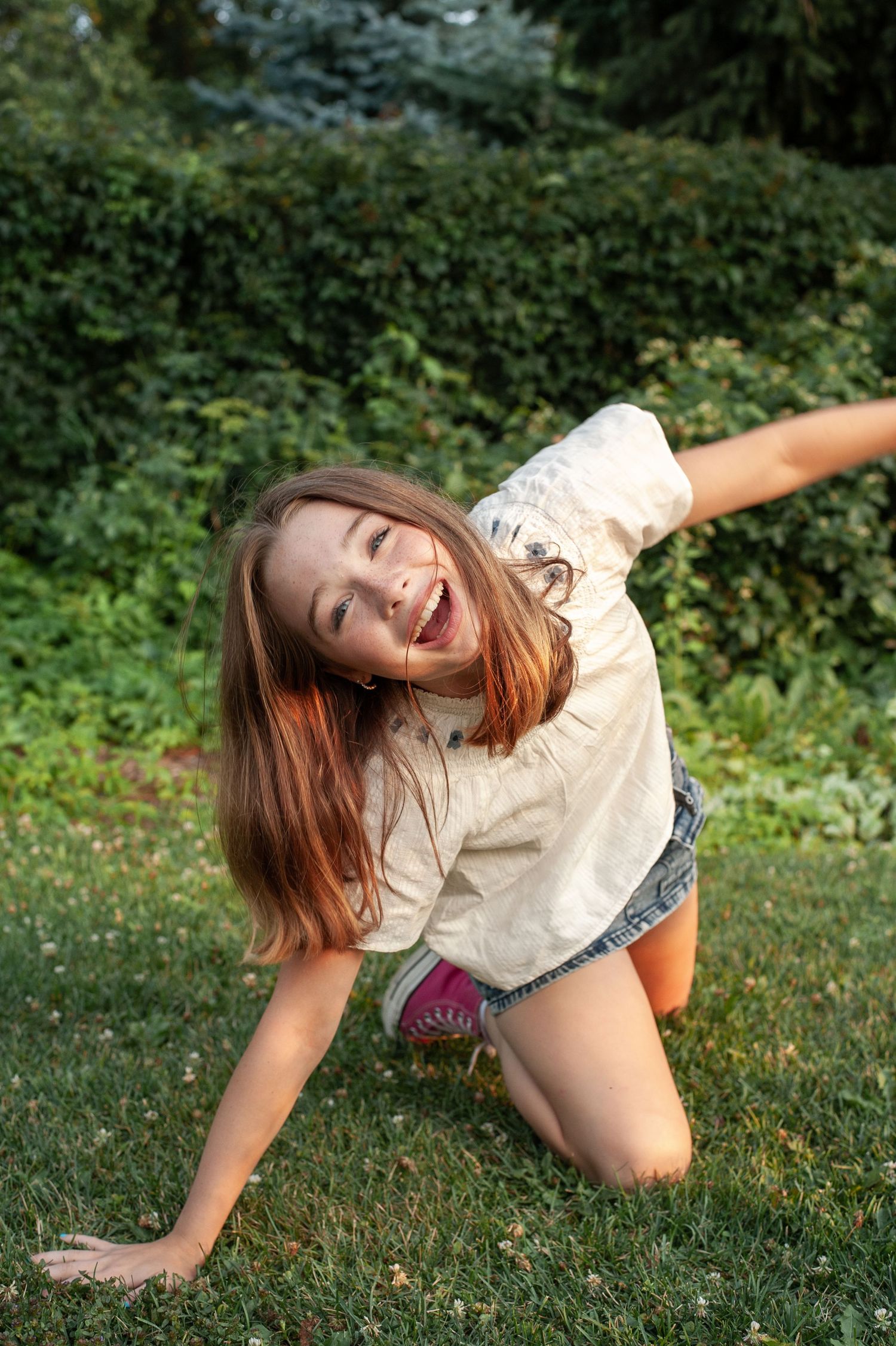 A person in casual attire strikes a fun pose while sitting on grass in a garden setting.