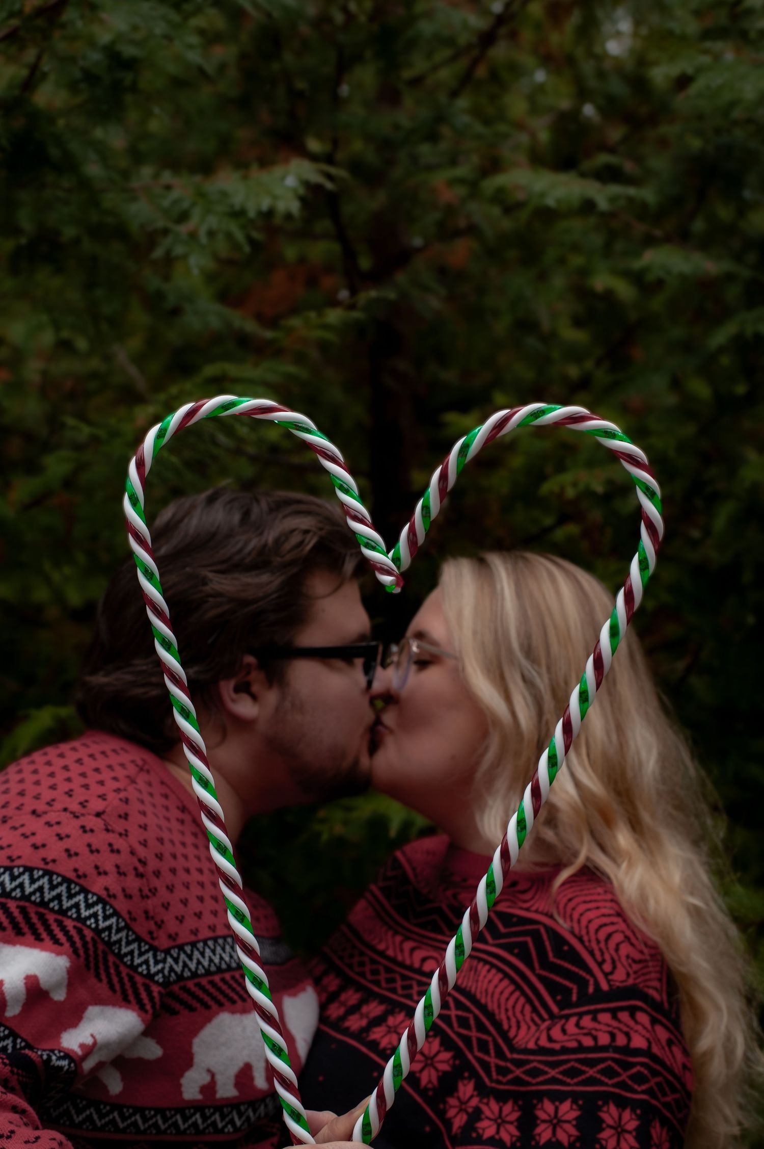 Couple in matching winter sweaters kiss behind candy canes forming heart shape.