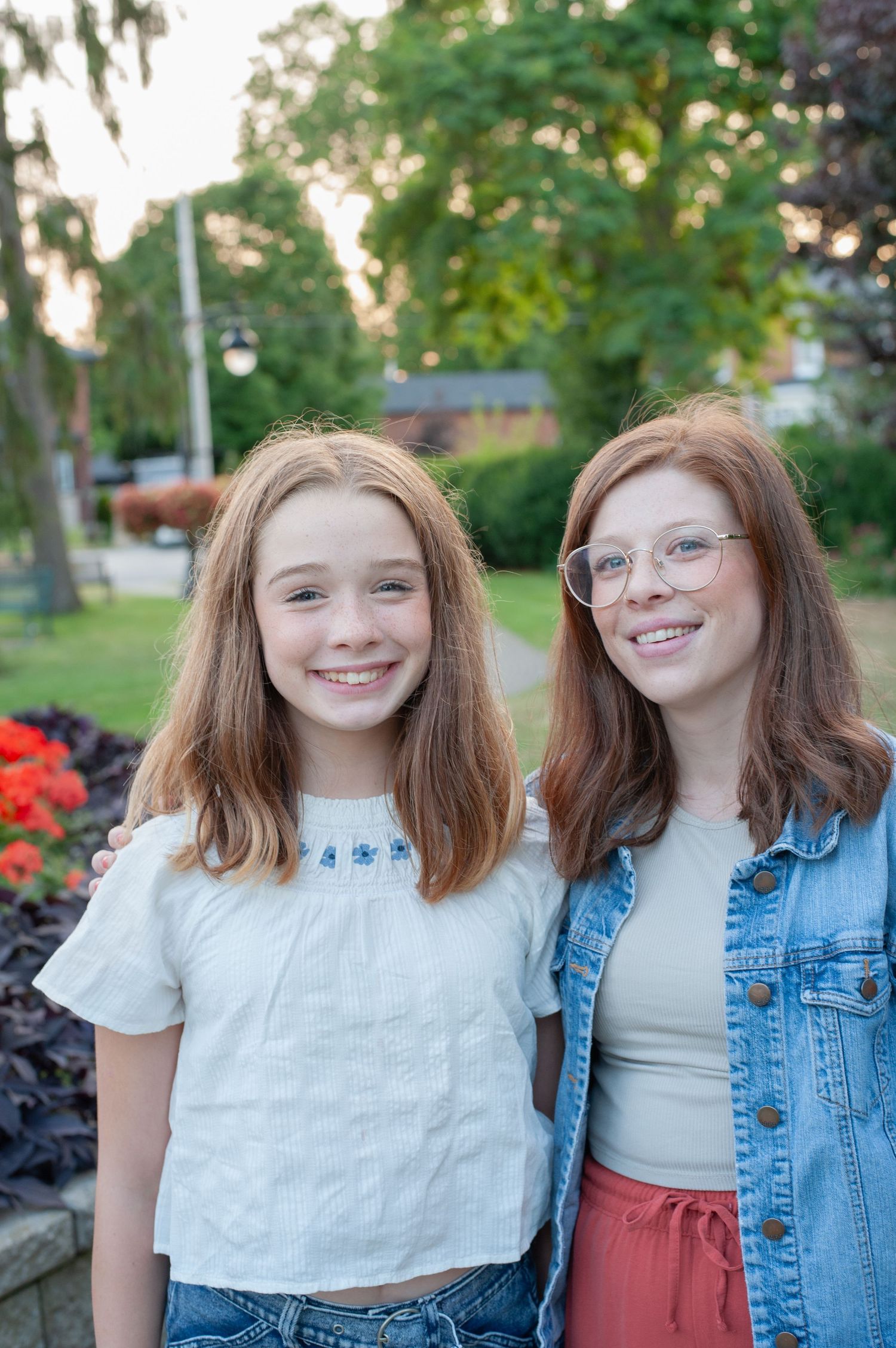 Two people in casual summer outfits smiling together outdoors with greenery in background.