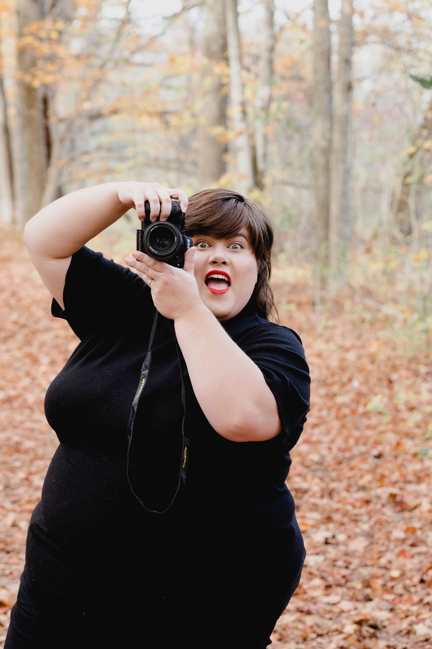 A photographer in a black sweater takes pictures in an autumn forest with fallen leaves on the ground.