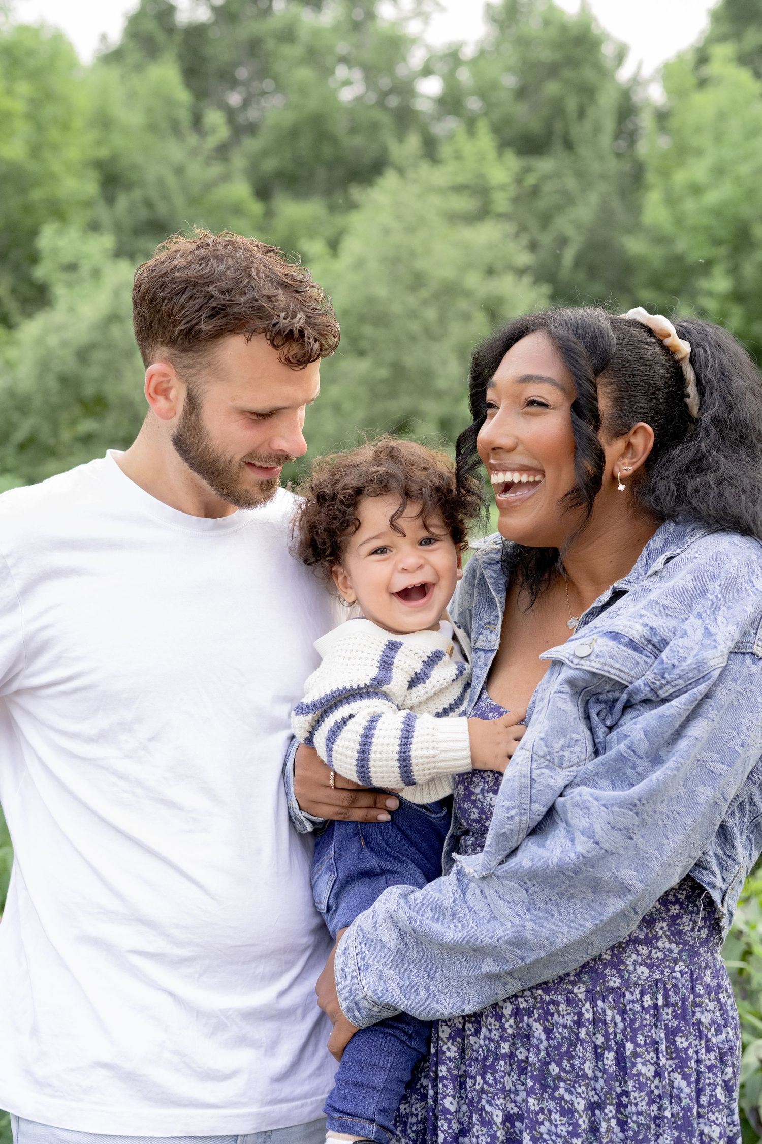 Family enjoying playful moments together outdoors in a natural setting with trees in background.