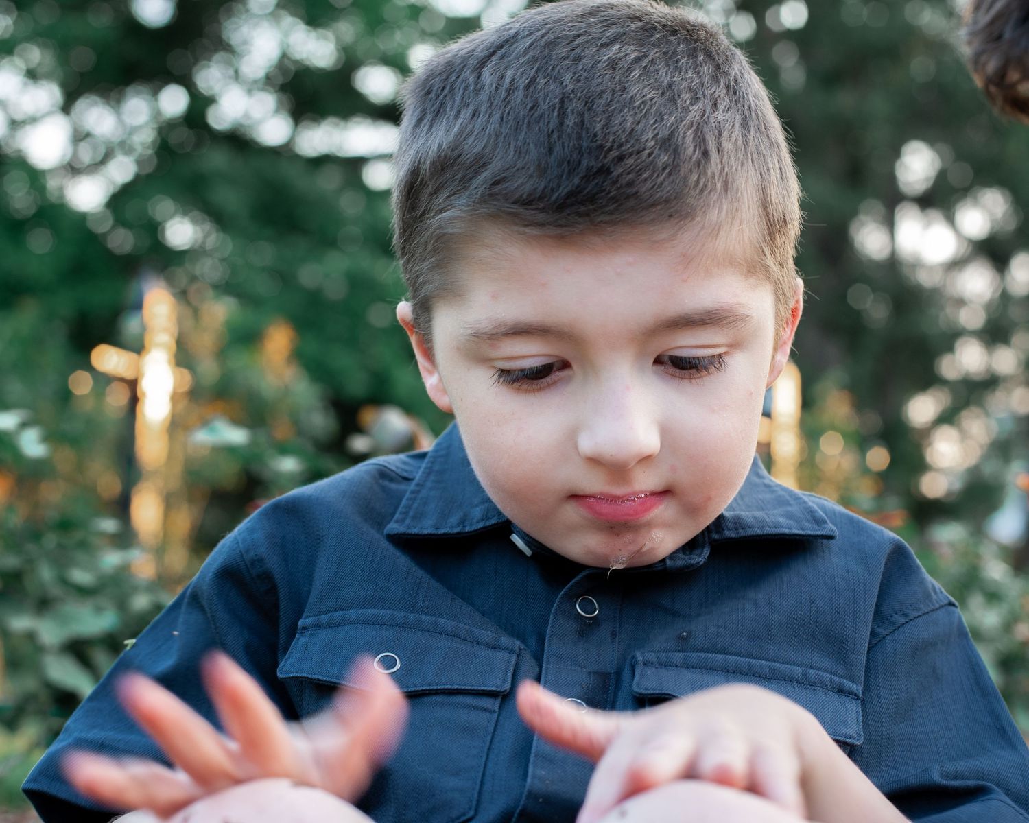 A young child in a navy blue shirt looks down while examining something in their hands.