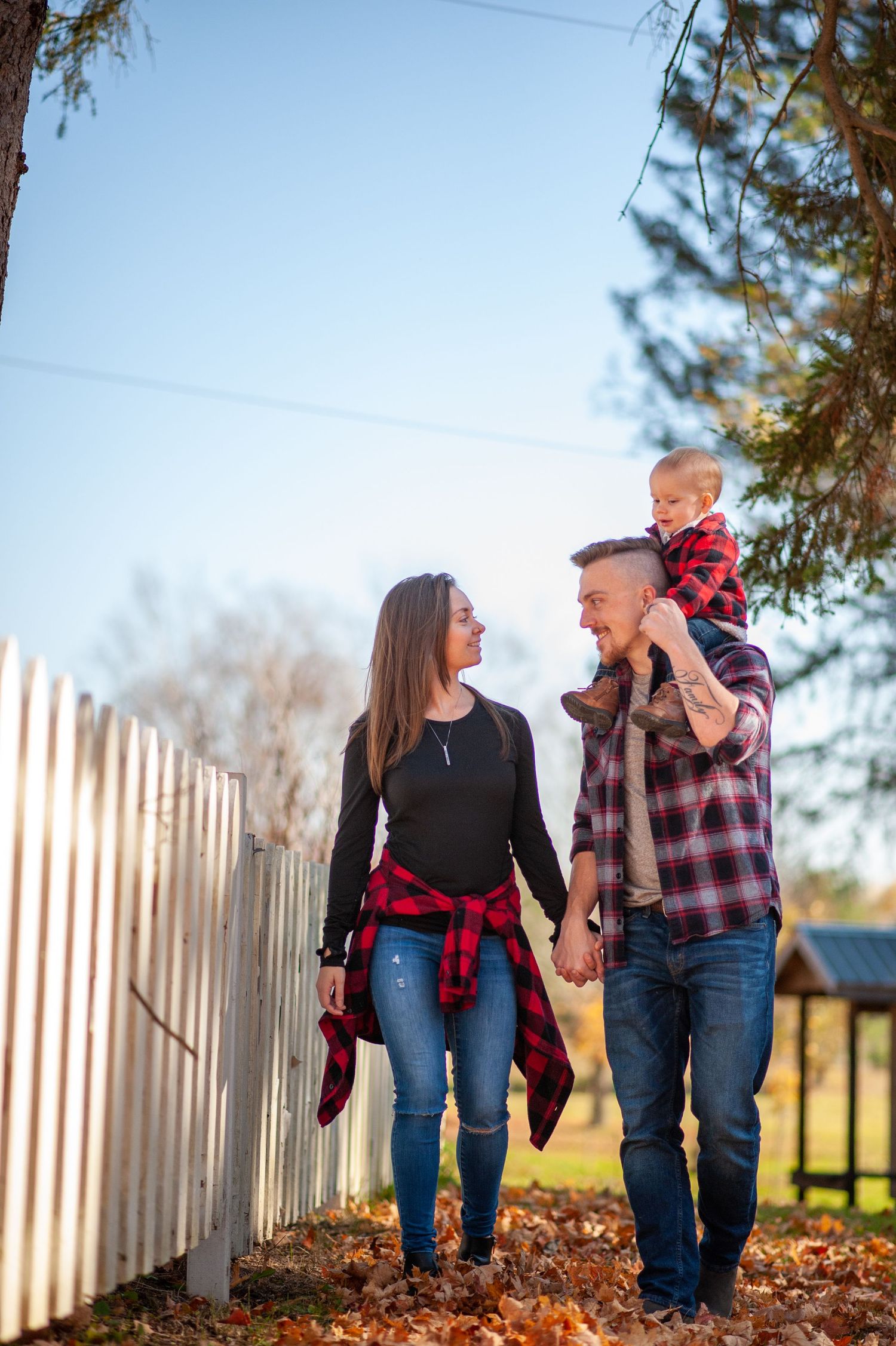 Family walking together along white picket fence on autumn day.