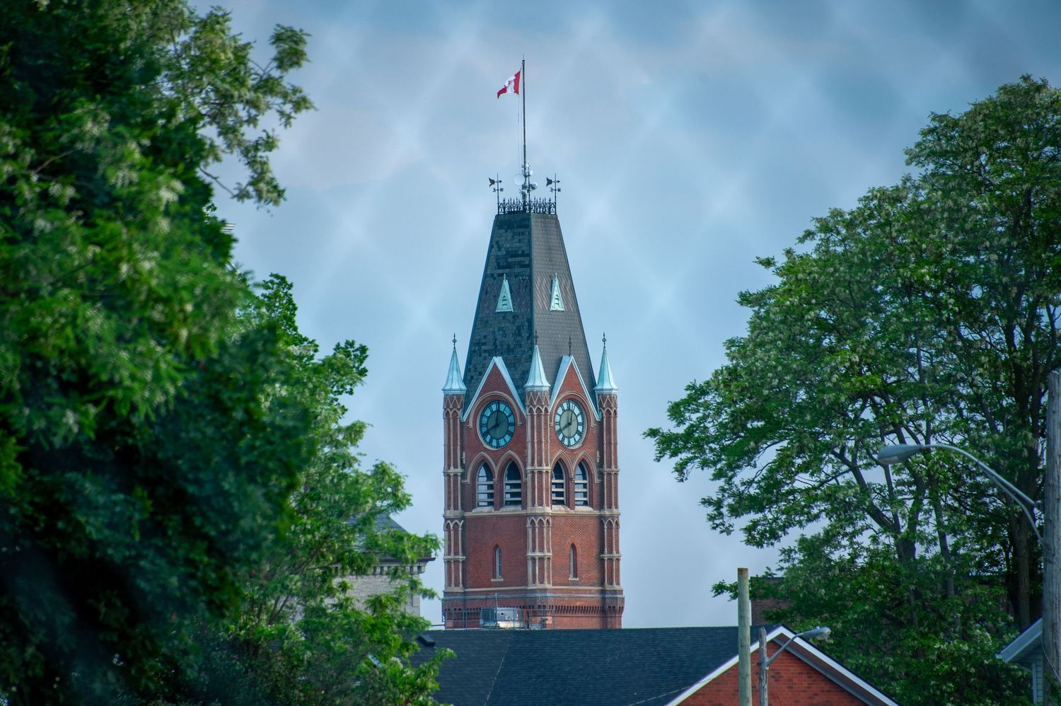 Gothic church tower with blue spire and Canadian flag against cloudy sky.