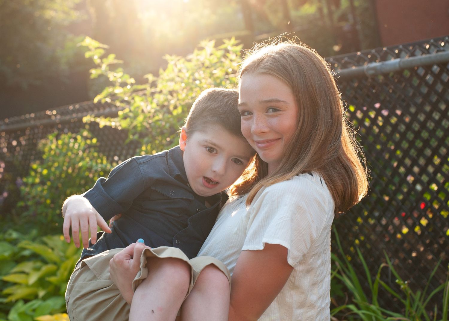 Sweet candid moments captured in warm backlit sunlight against a garden setting.