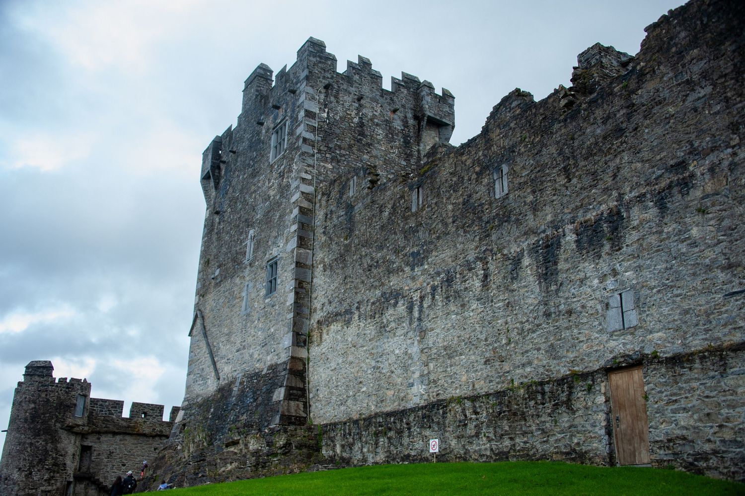 Imposing stone castle walls and towers rise against a cloudy sky in Ireland.