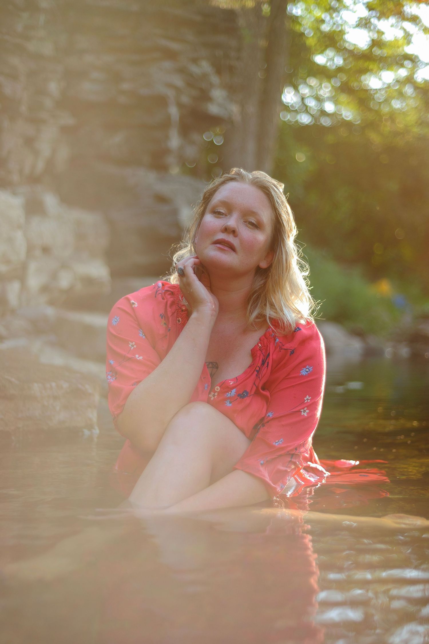 Woman in coral dress poses thoughtfully in sunlit water.