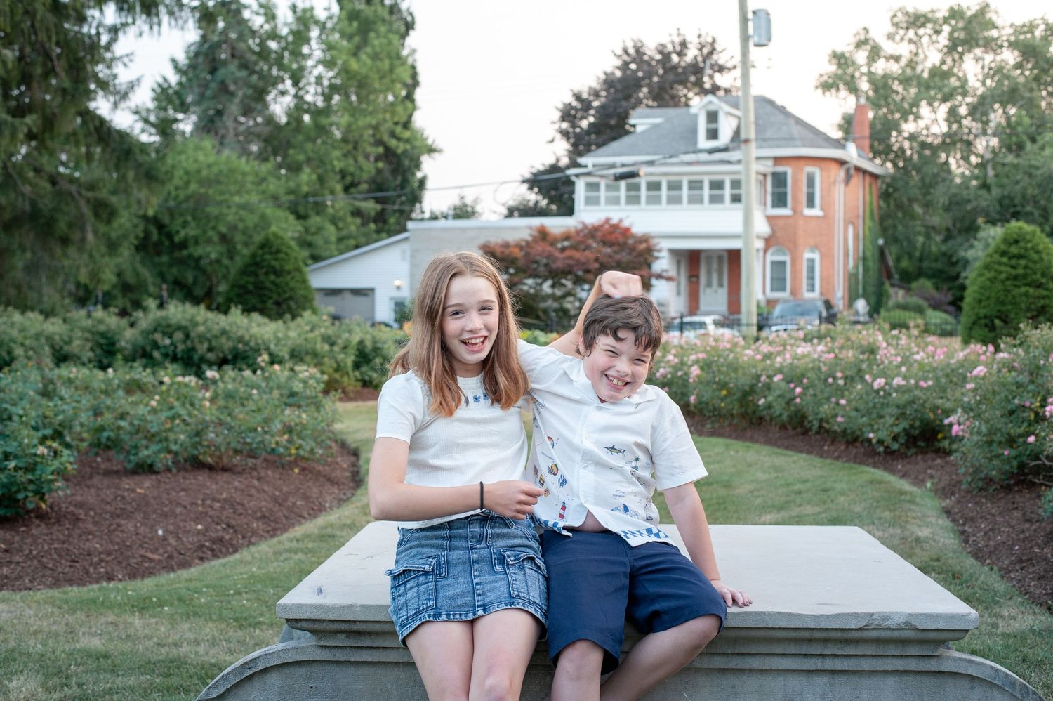 Children sitting and laughing together on outdoor stone steps surrounded by lush gardens and landscaping.