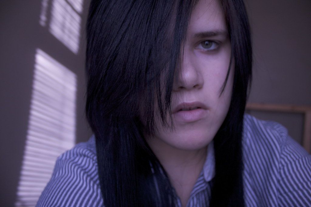 A moody portrait shot through window blinds with dramatic lighting.