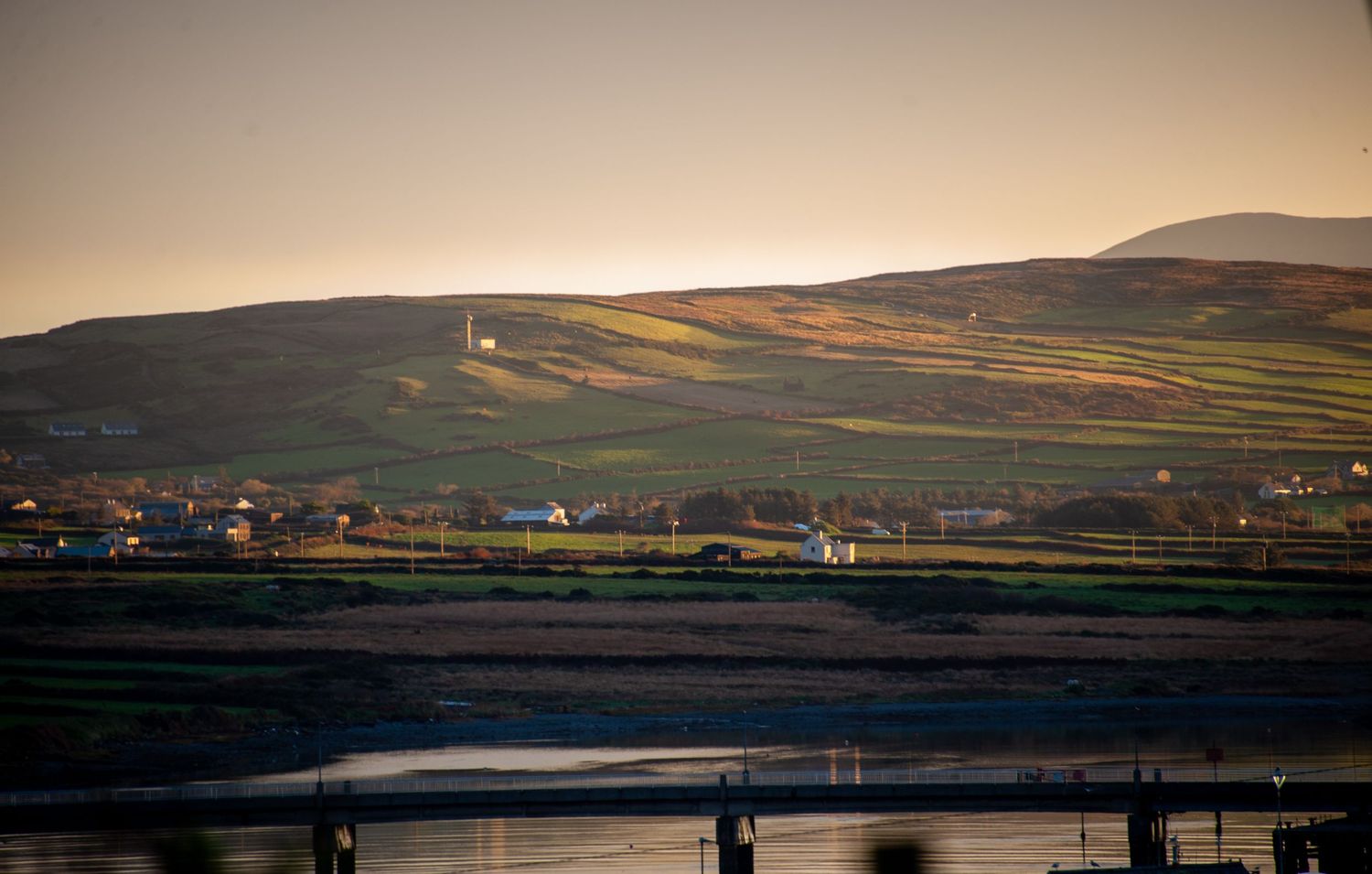 Panoramic view of a rural valley with bridge and distant hills at sunset.
