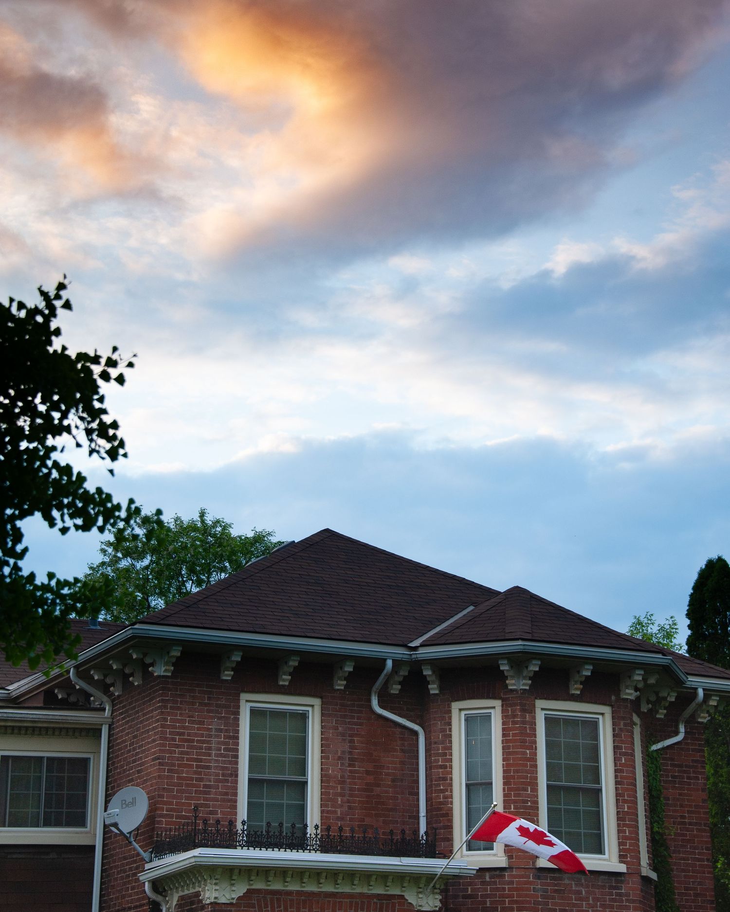 Red brick house with pitched roof and decorative trim against sunset sky.