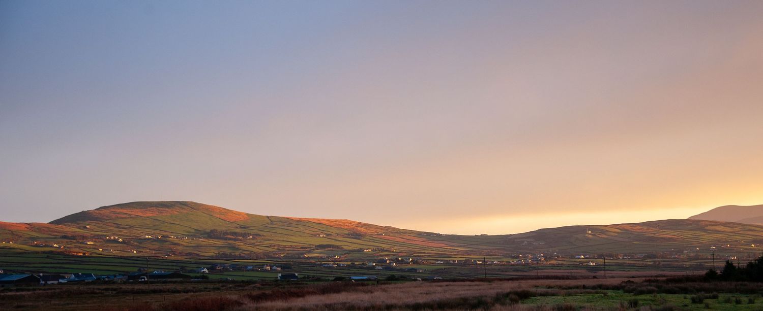 Wide panoramic view of mountains at dusk with golden sunset colors in the sky.