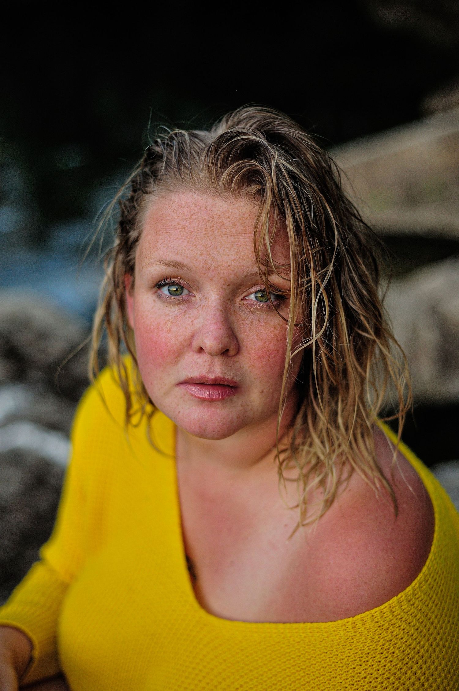 Portrait of a woman in a yellow sweater with wet hair against a rocky backdrop.