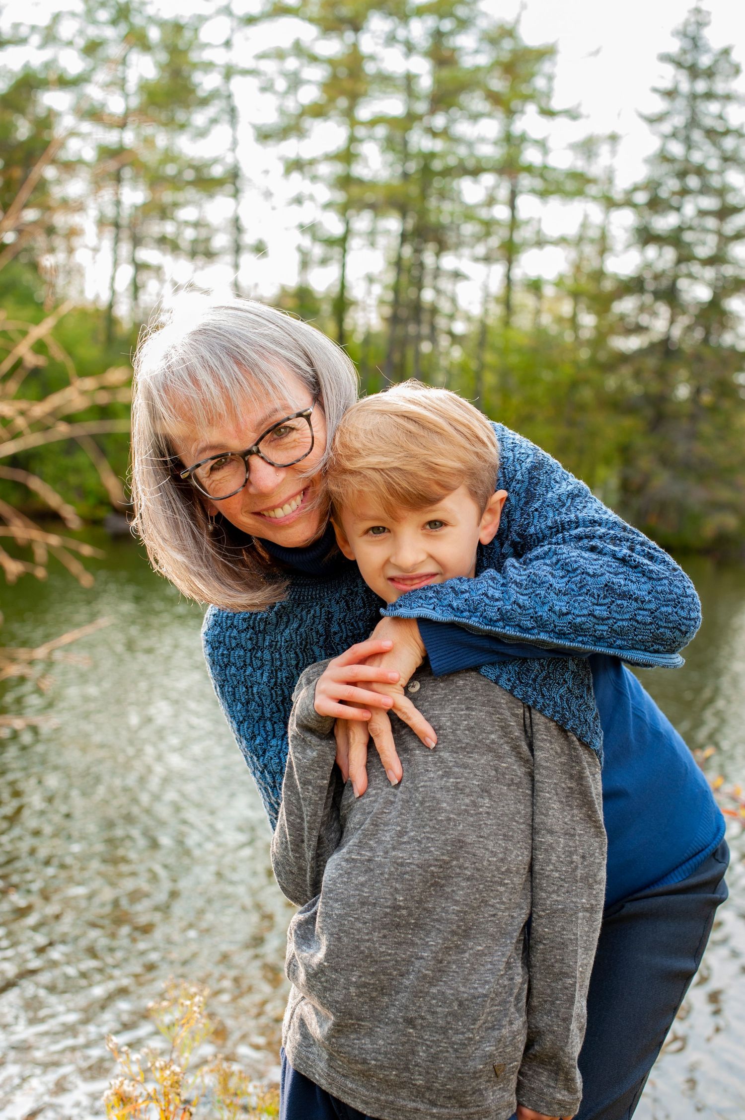 Heartwarming moment between two people embracing by a lake with pine trees in background.