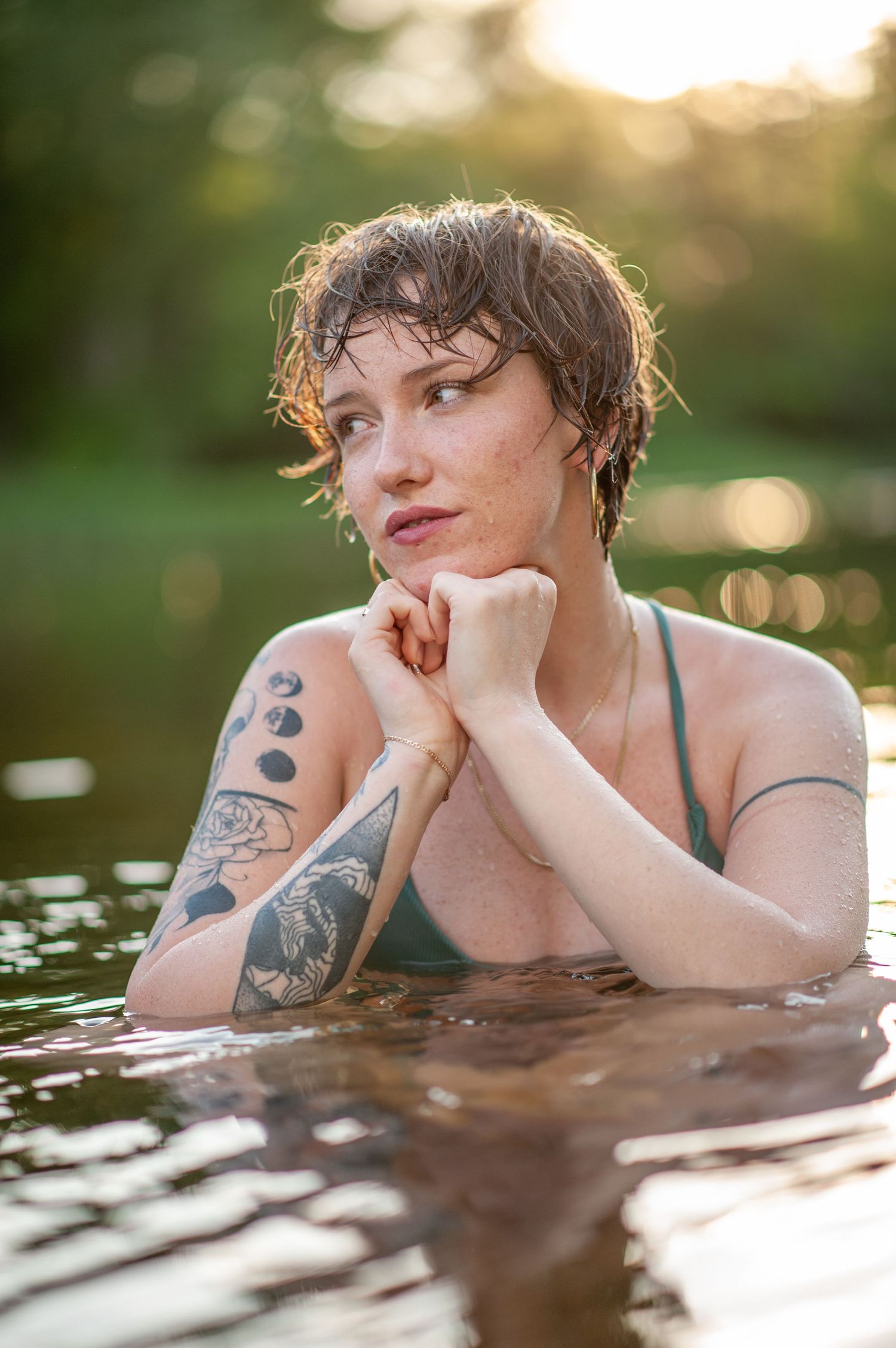 Artistic portrait of someone with short hair and tattoos partially submerged in water at sunset.