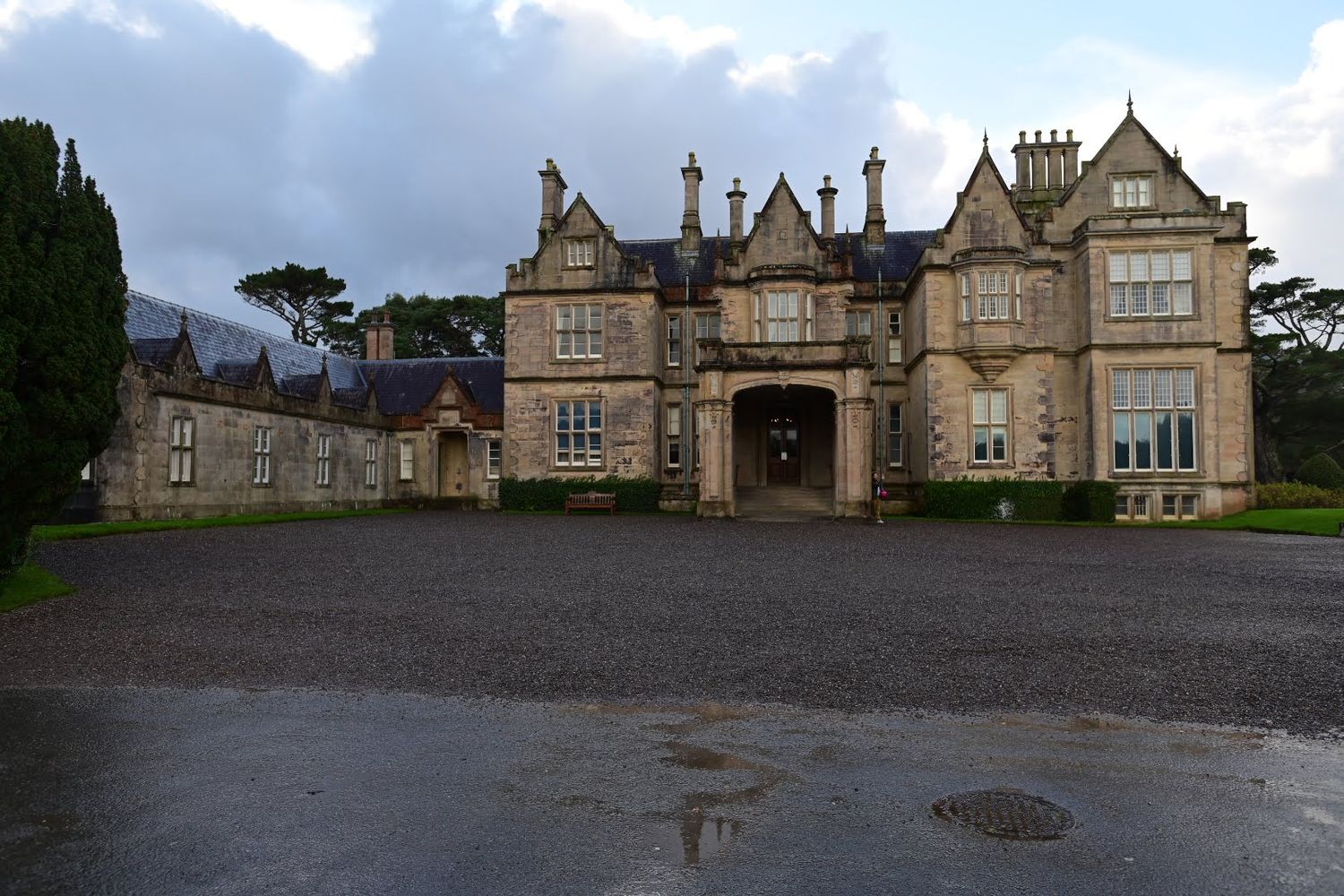 Gothic revival manor house with stone facade and central entrance portico on a rainy day.