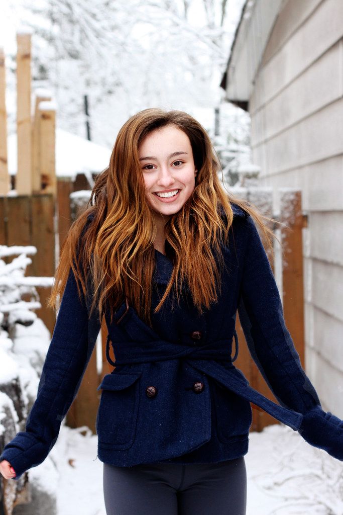 Winter portrait of someone in a navy blue coat standing against white snow and siding.