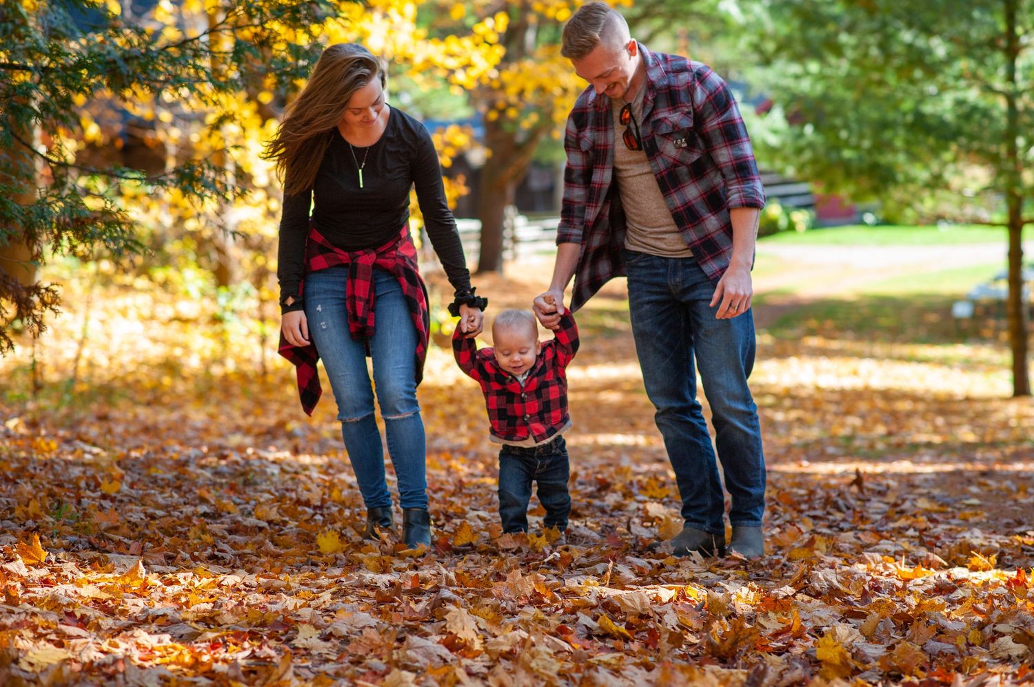 Family members walk together on fallen autumn leaves in a park setting during fall season.