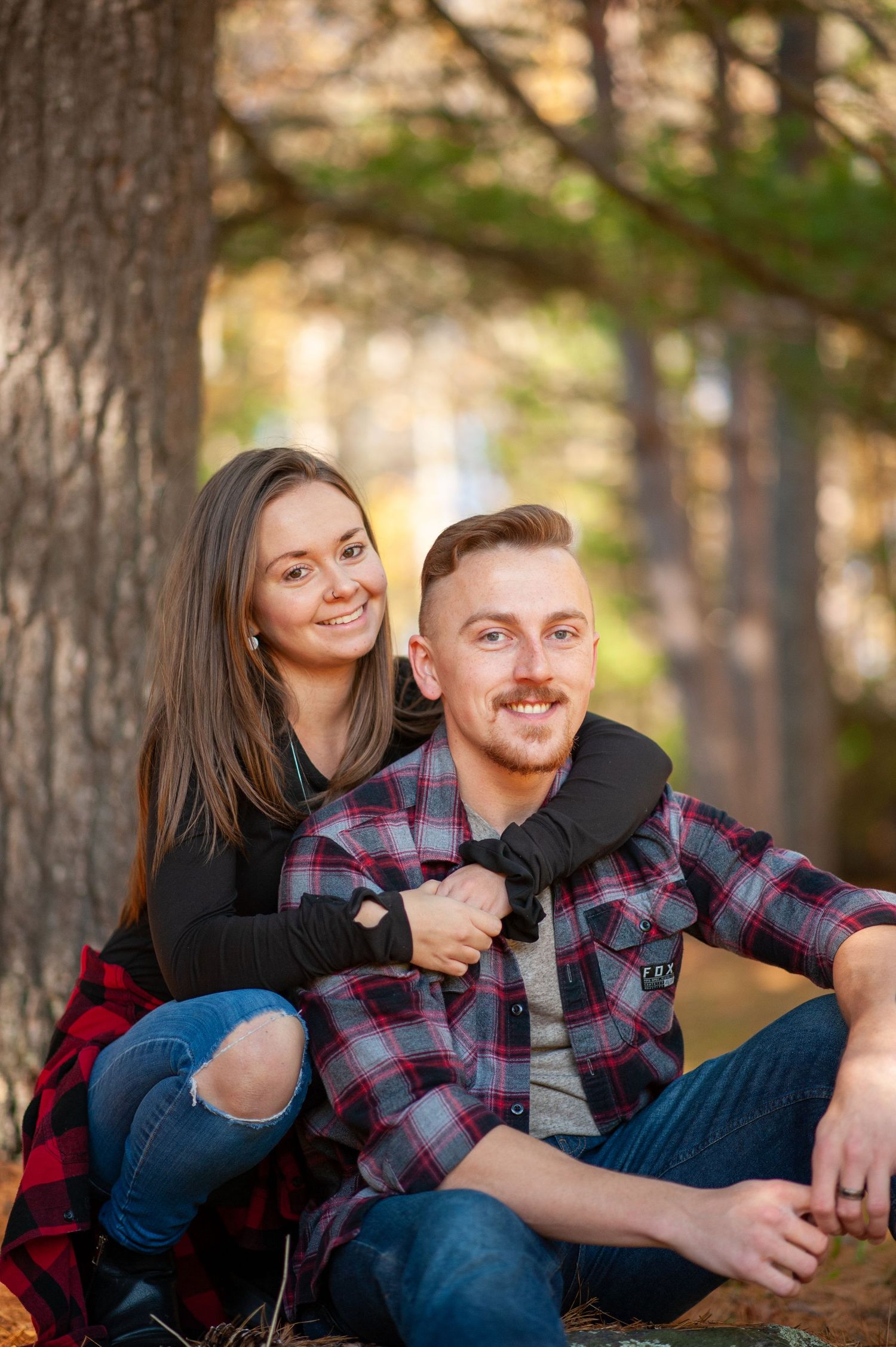 Couple relaxing outdoors against tree trunk in casual autumn attire.