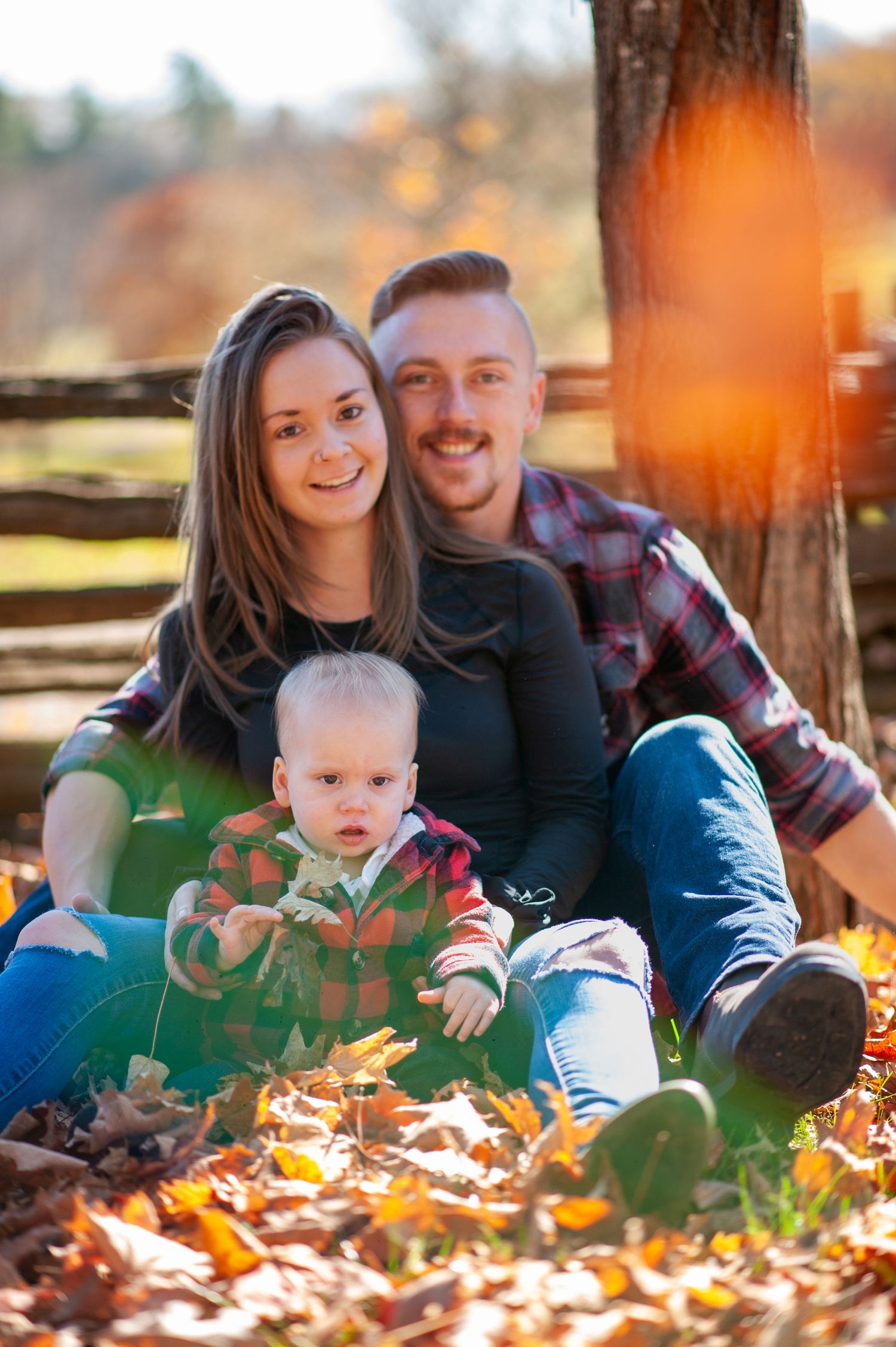 Family sitting together among fall leaves during sunset outdoors.