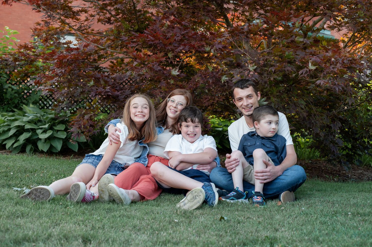 A family relaxes together on a green lawn with colorful autumn foliage in the background.