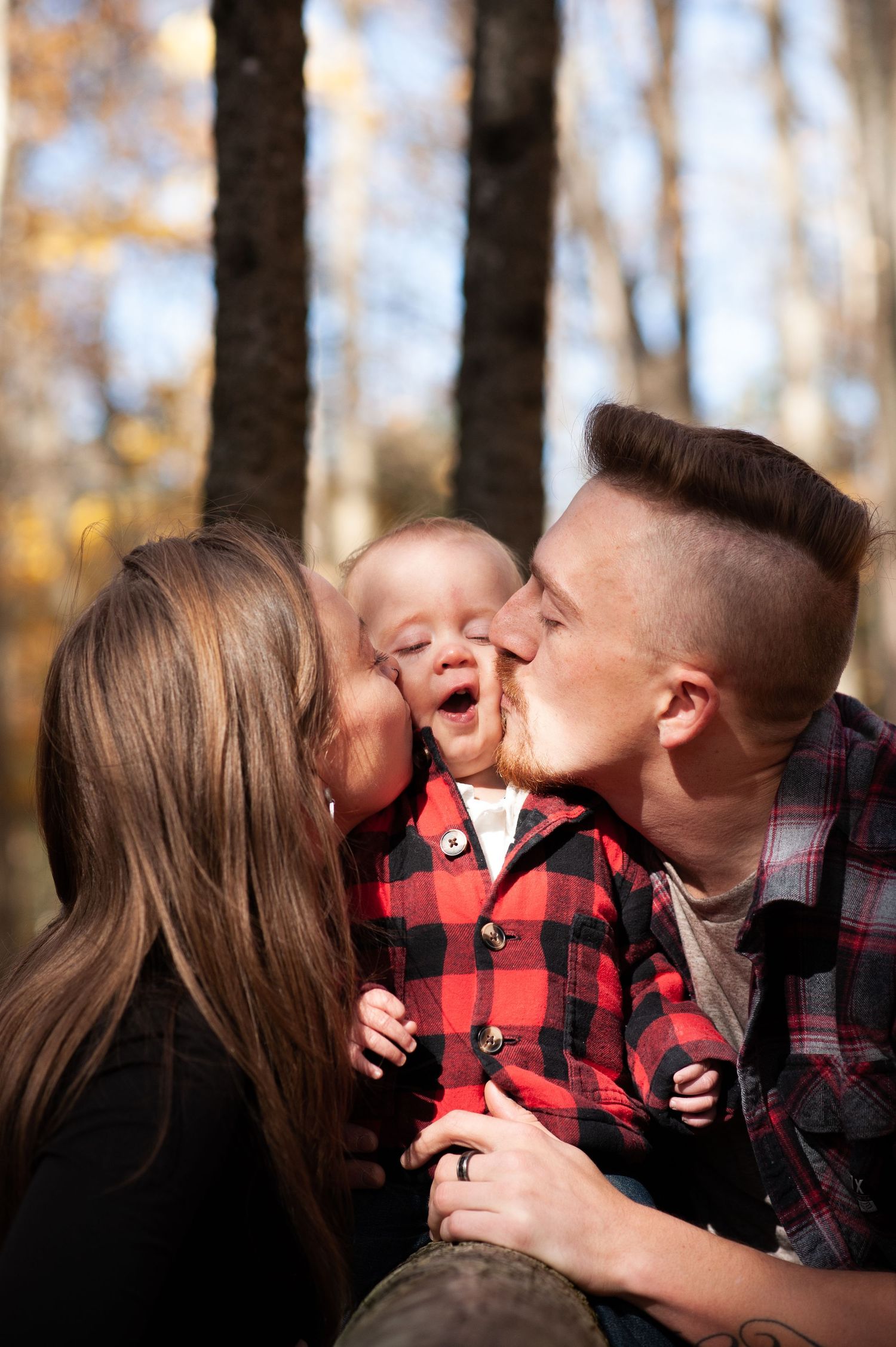 Family sharing tender moment outdoors with fall trees in background.